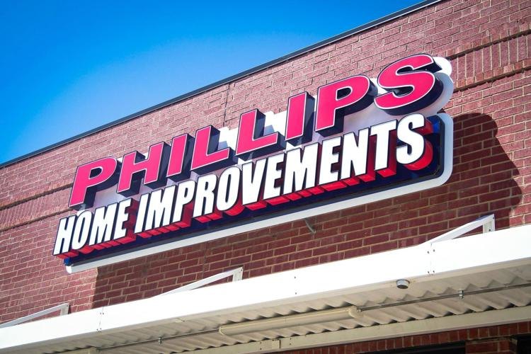 Exterior brick building with a large red and white Phillips Home Improvements sign against a blue sky.