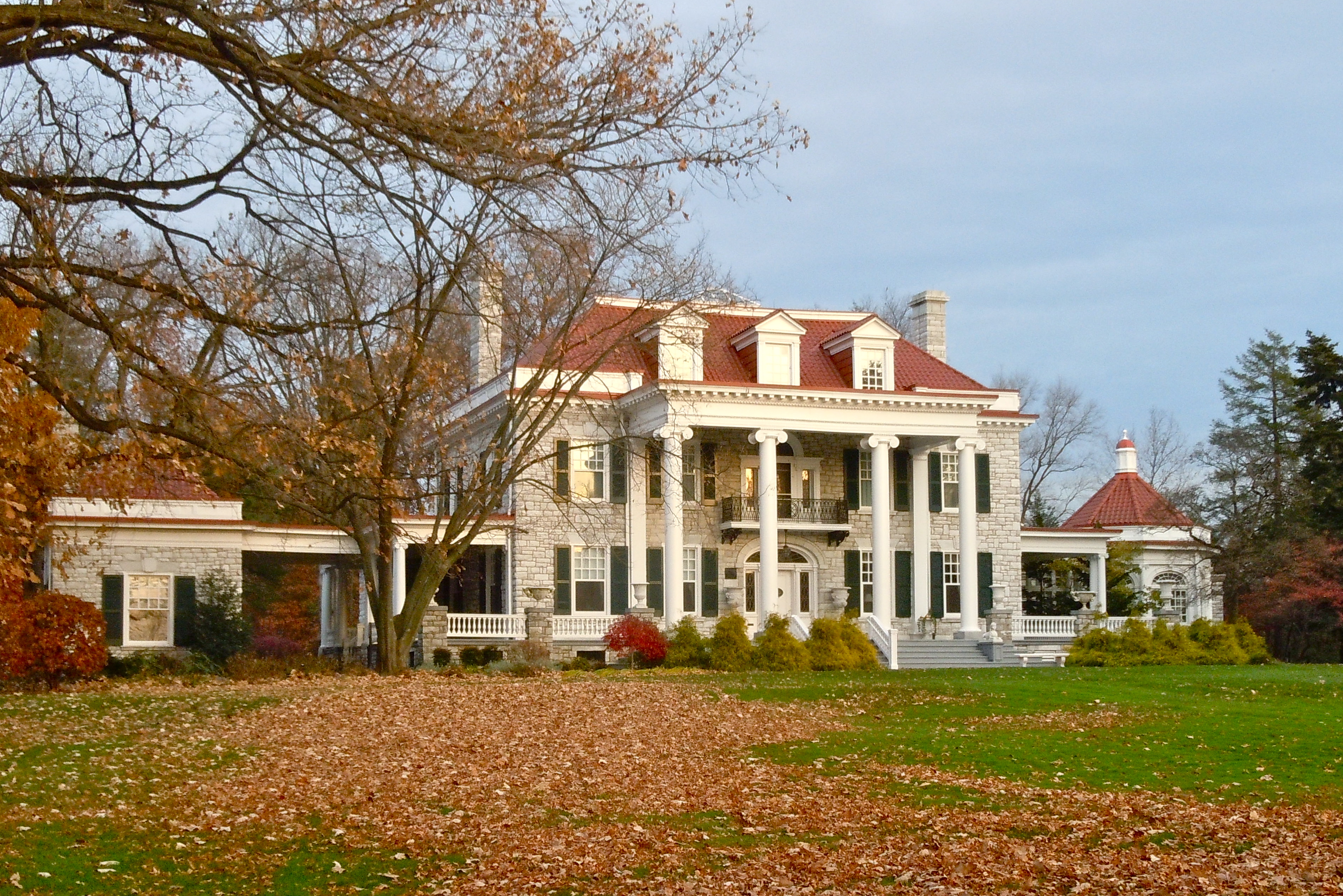 Large white neoclassical mansion with columned portico surrounded by autumn foliage.