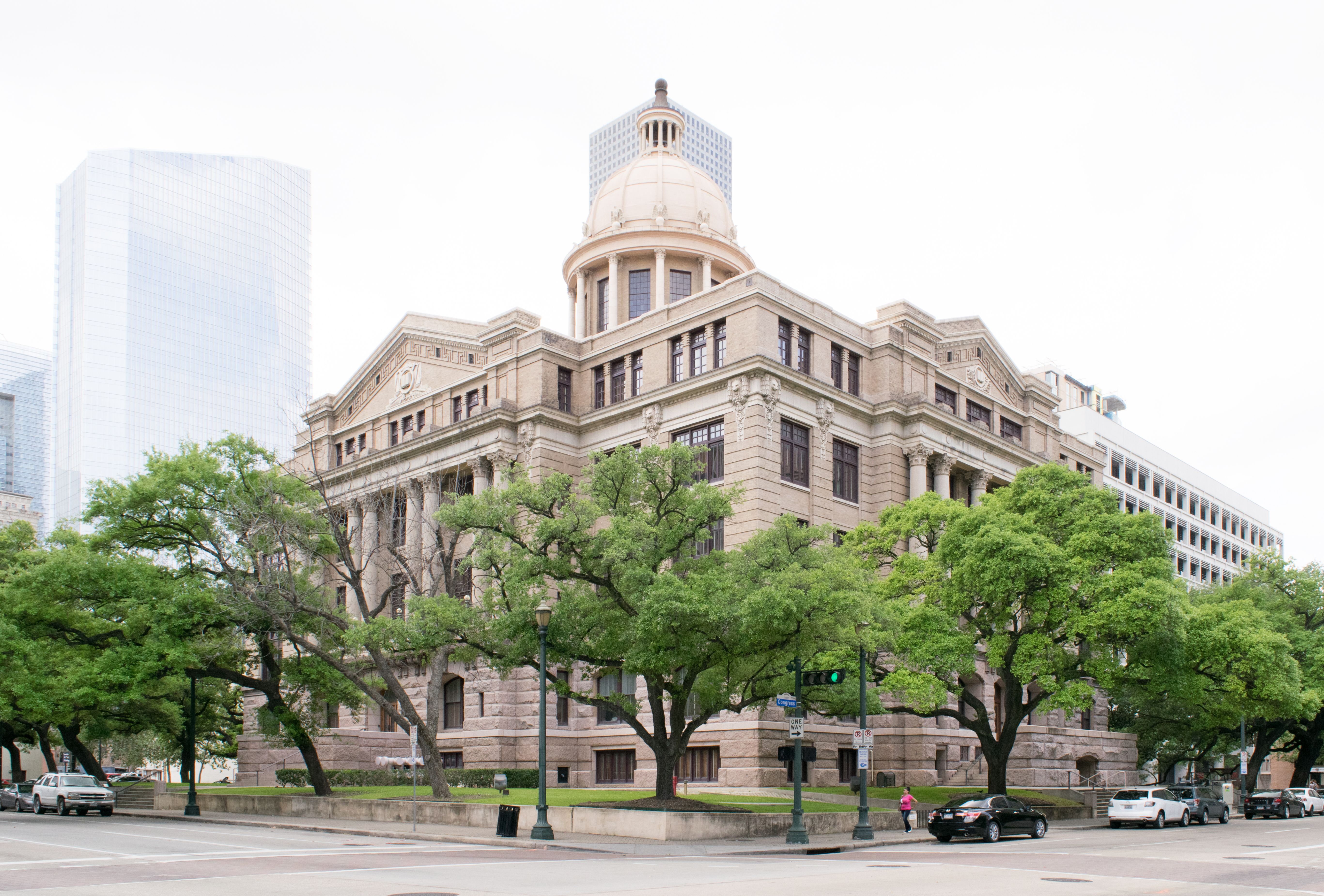 Historic domed stone courthouse at a street corner with a glass skyscraper behind it.