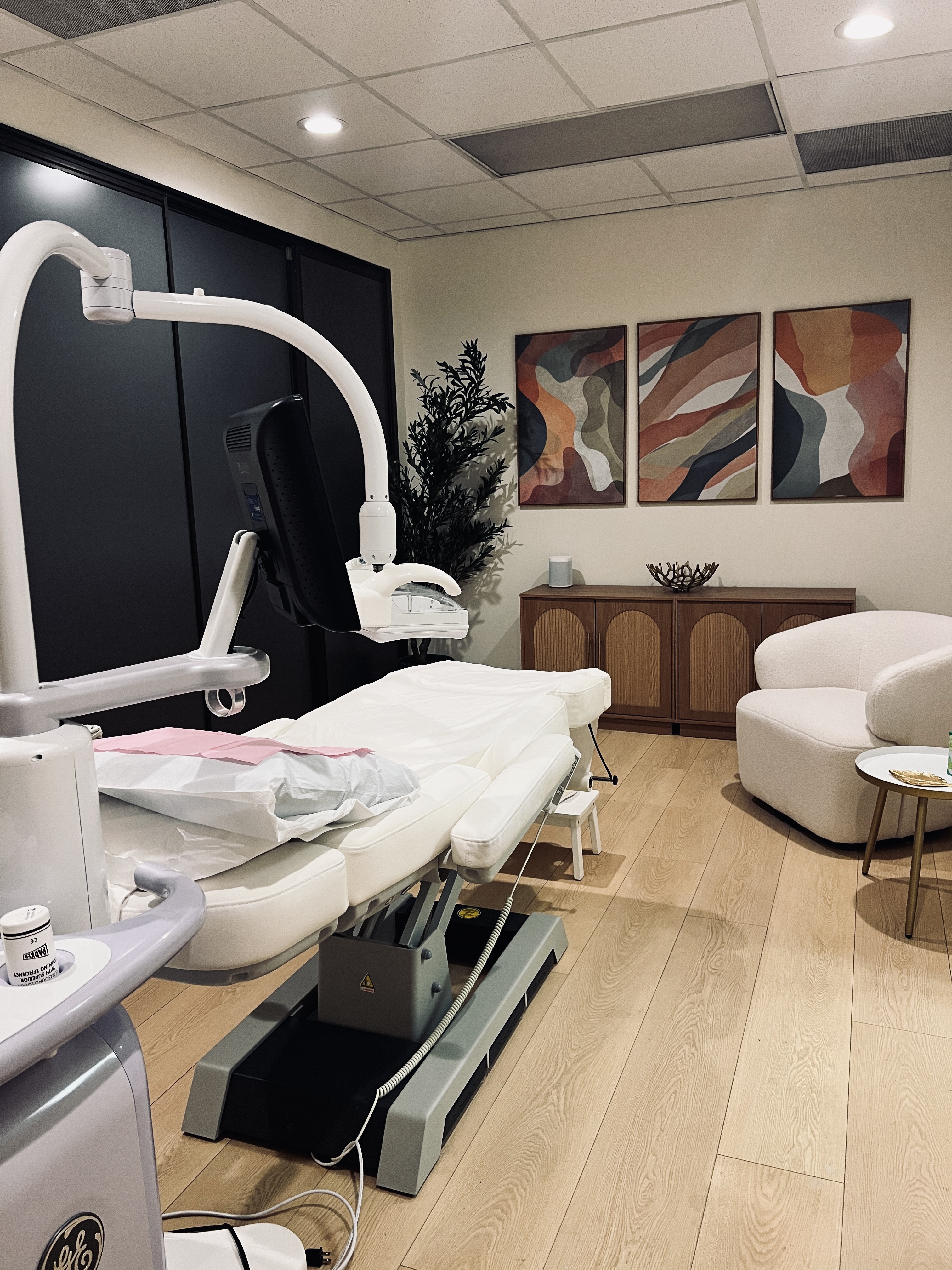 Ultrasound equipment beside a padded examination table in a room with abstract artwork.