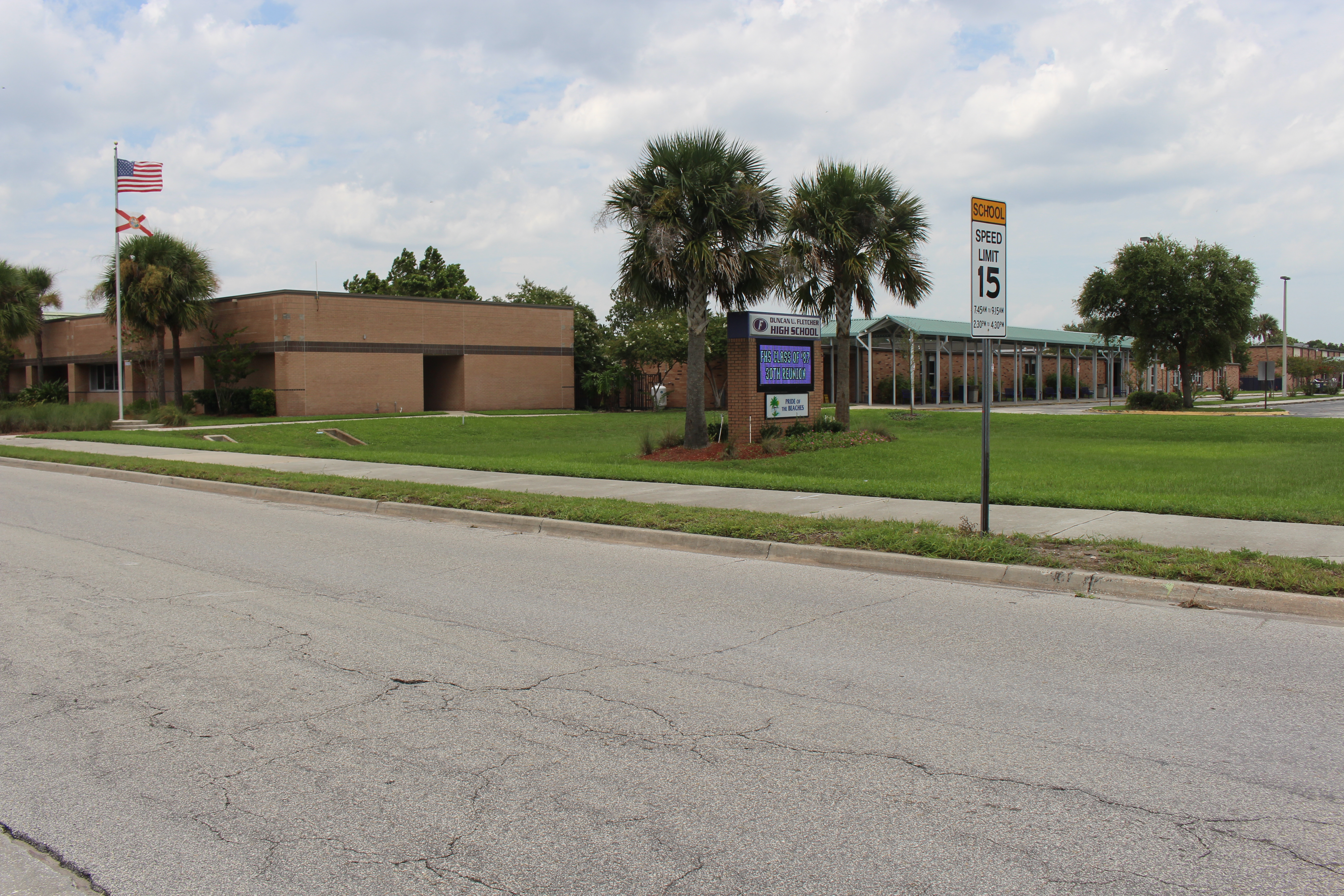 Single-story brick school building with palm trees and two flags out front.