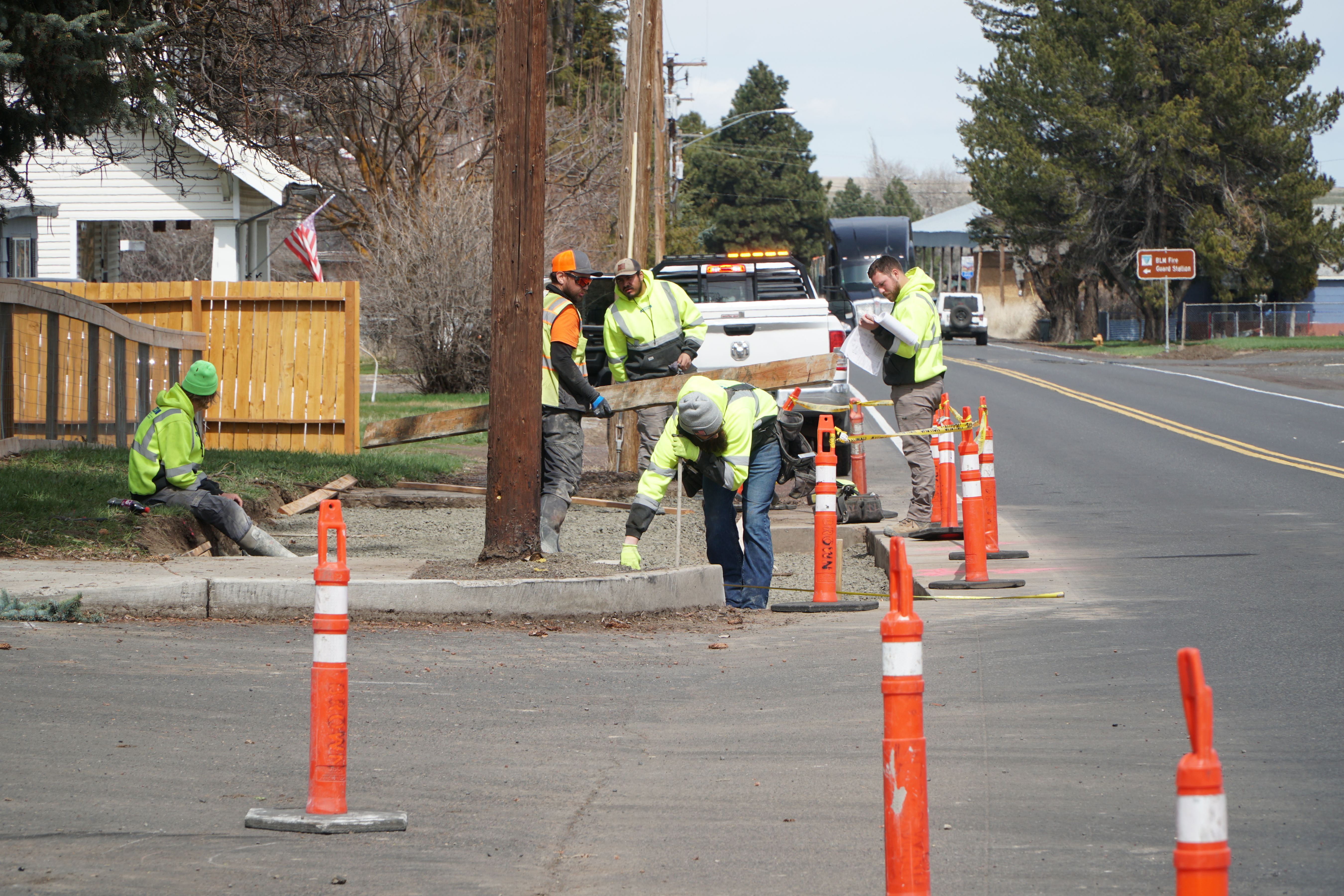 Workers in safety vests and hard hats repairing a curb ramp along a residential street.