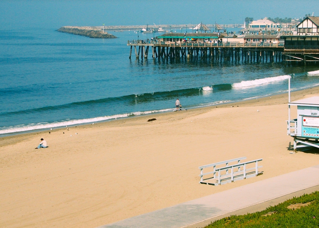 Sandy beach with a wooden pier extending into calm blue ocean water.