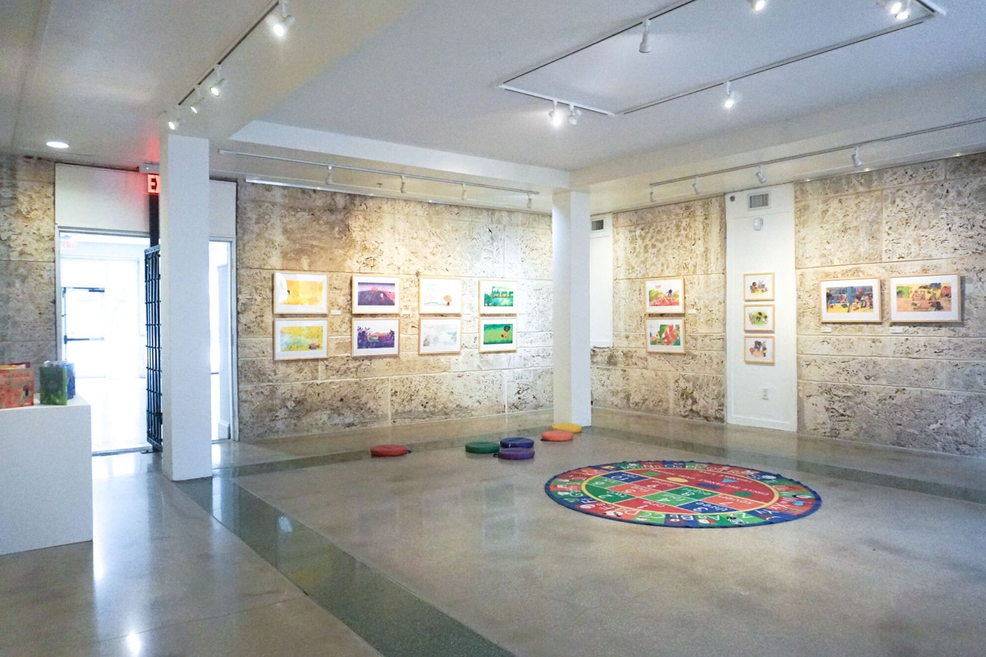 Gallery interior with colorful framed artworks on stone walls and a circular patterned floor piece.