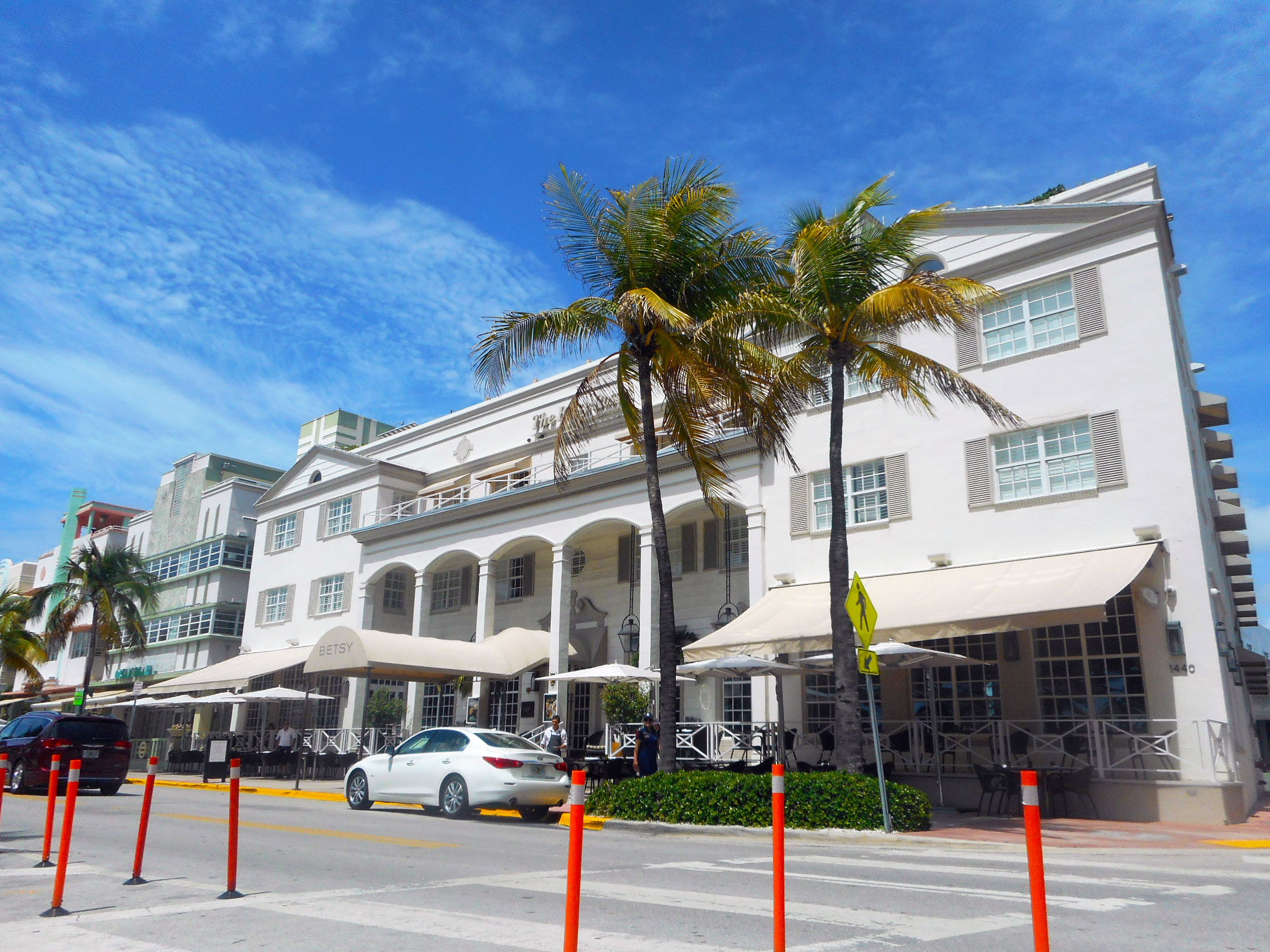 White Art Deco hotel with arched colonnades and palm trees along a sunny street