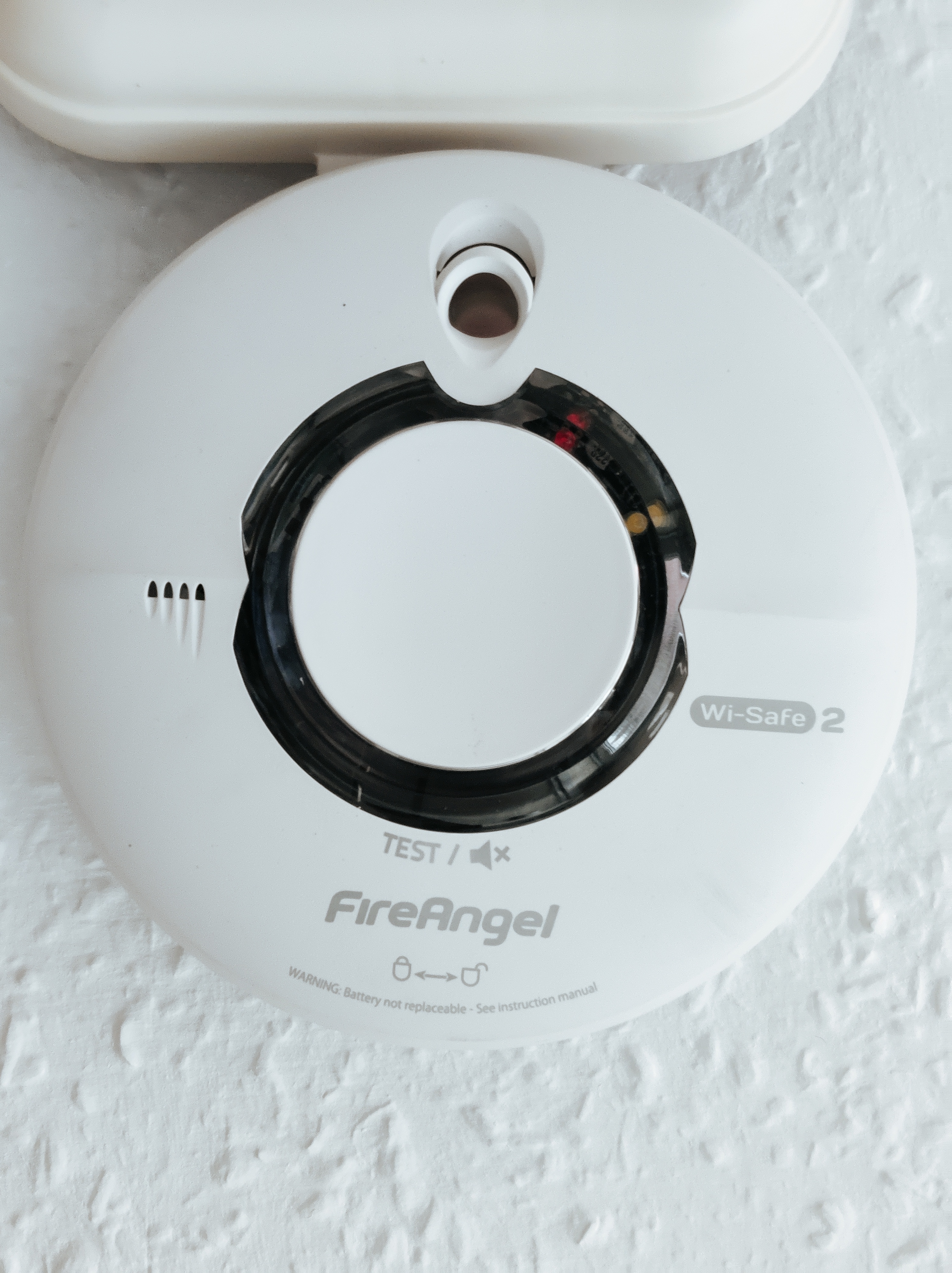 A circular smoke detector removed from its ceiling mount, next to an older square detector.