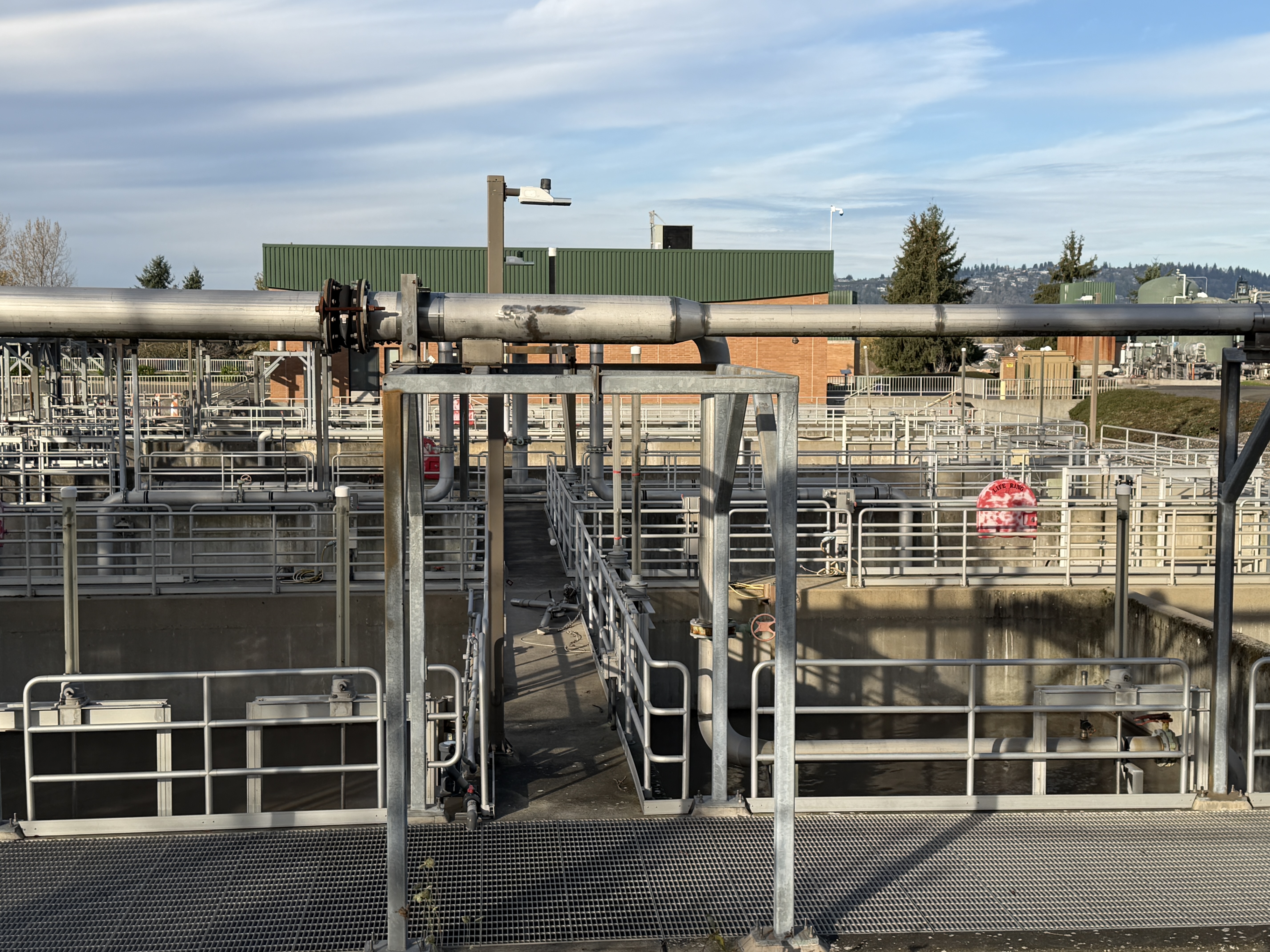 Aeration basins with large overhead pipes and metal grating walkways at a wastewater plant.