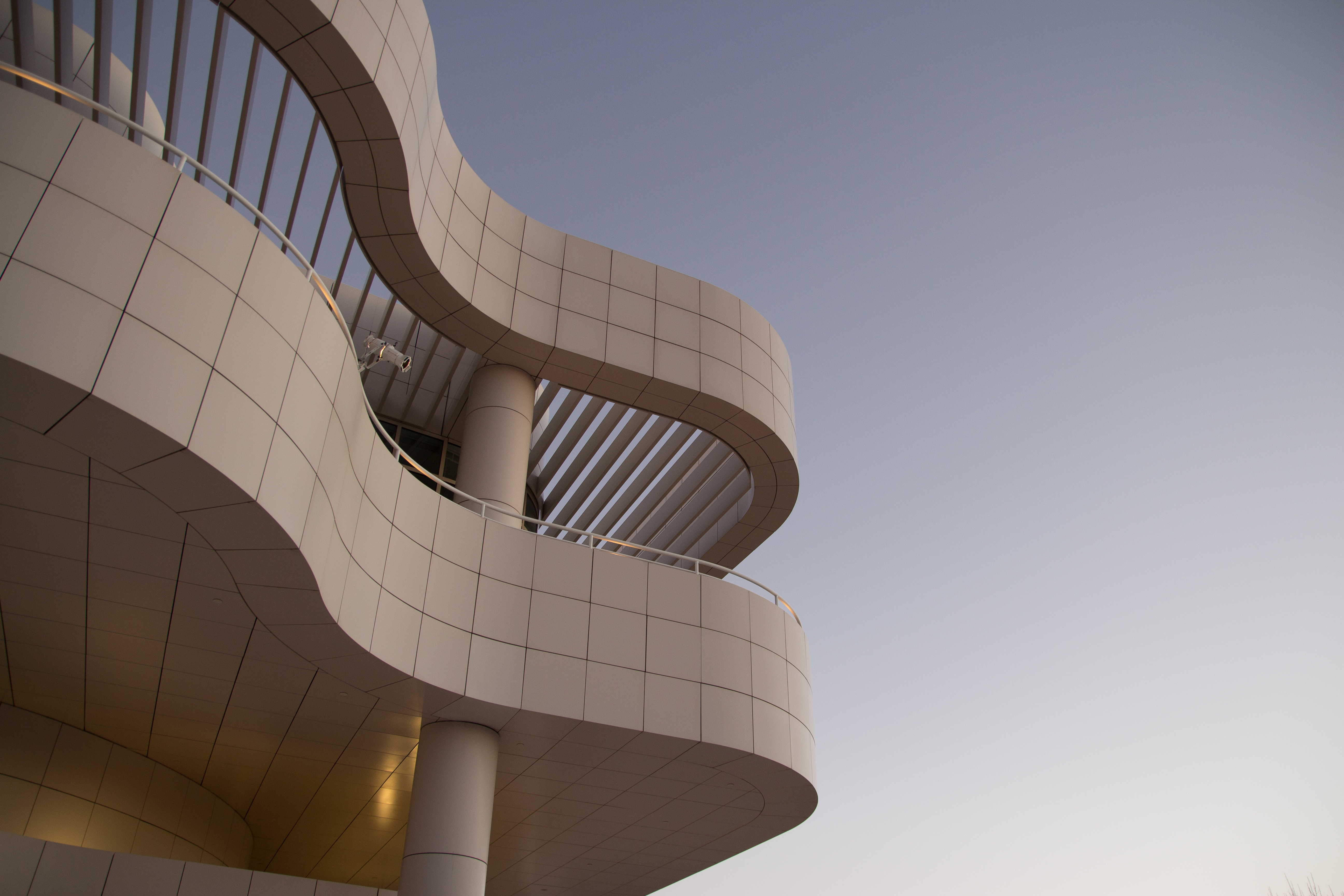 Curved white stone exterior of a modernist building viewed from below against a hazy sky.