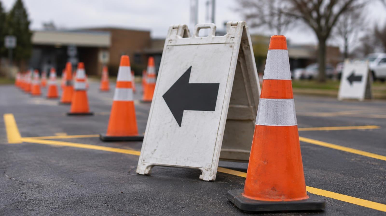 Orange traffic cones and arrow signs beside freshly painted yellow lane markings in a parking lot.