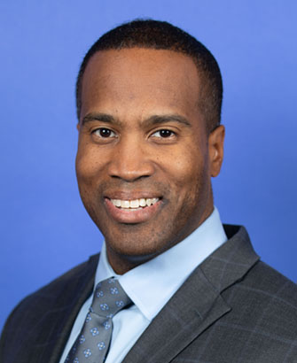 Man in gray suit and blue tie smiling in a professional headshot portrait.