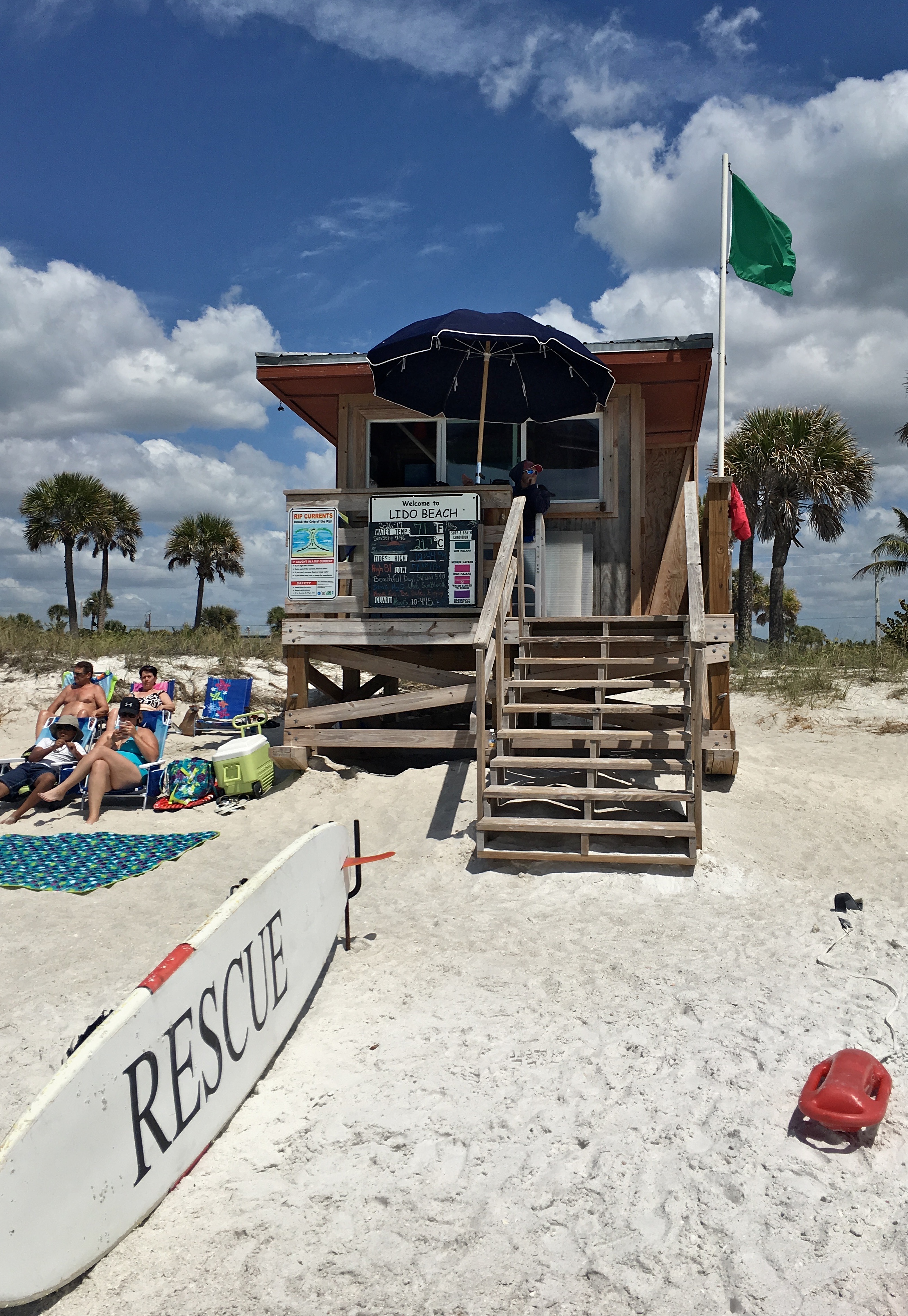Wooden lifeguard tower labeled Lido Beach with a rescue surfboard in the sand