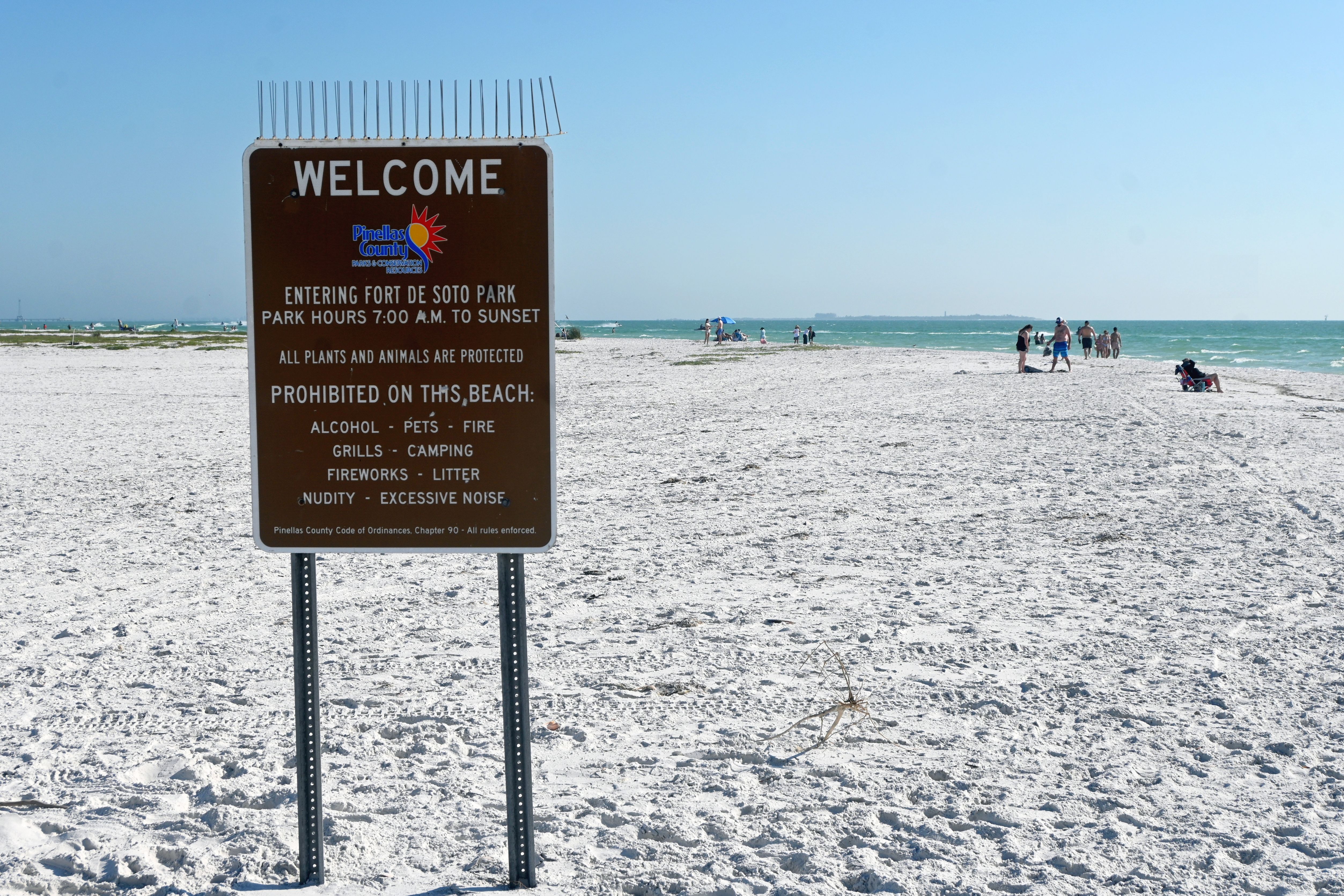 Brown park rules sign at a sandy Florida beach with beachgoers in the background.