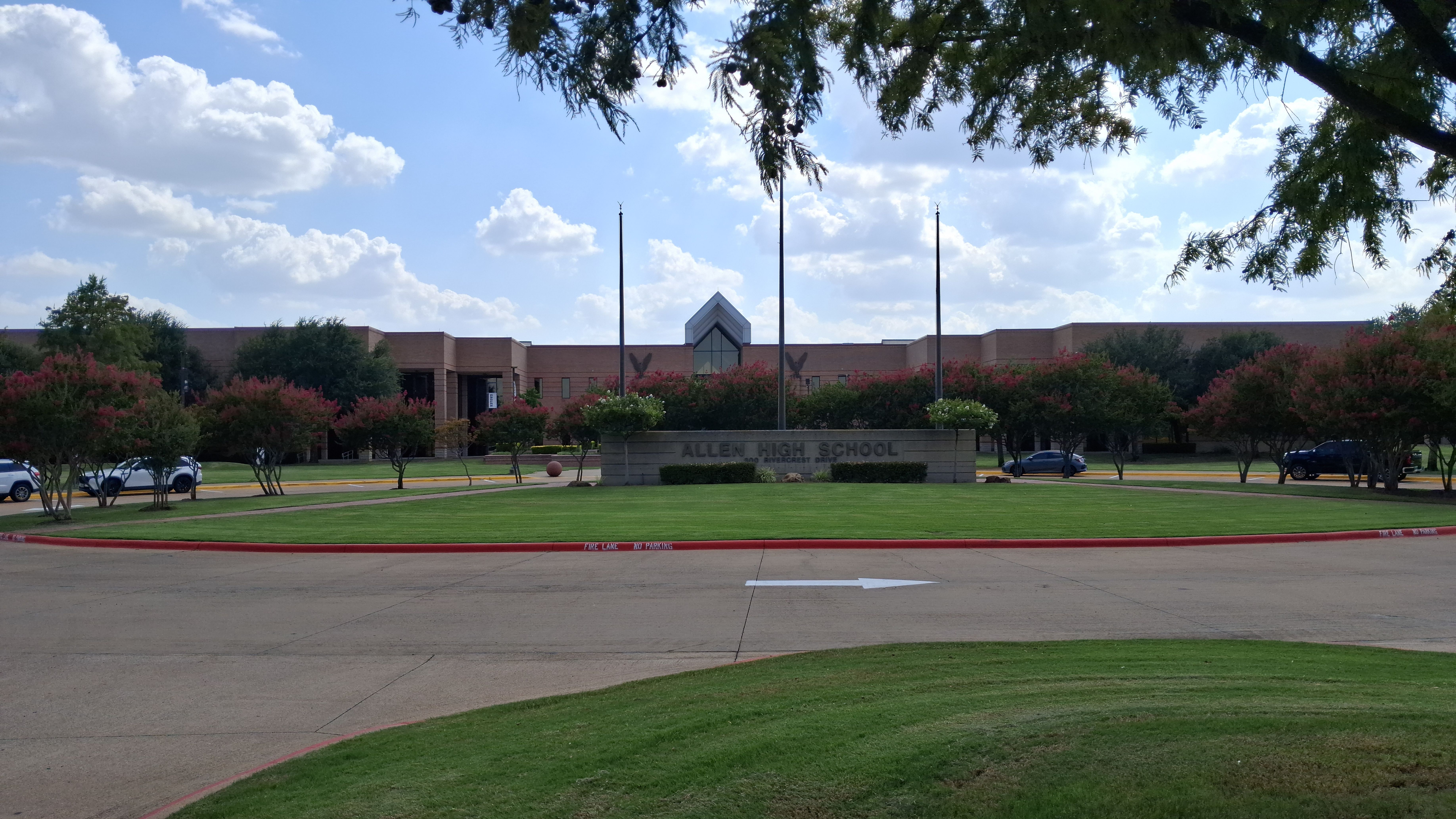 Brick school building with flagpoles and a sign reading Allen High School on a partly cloudy day.