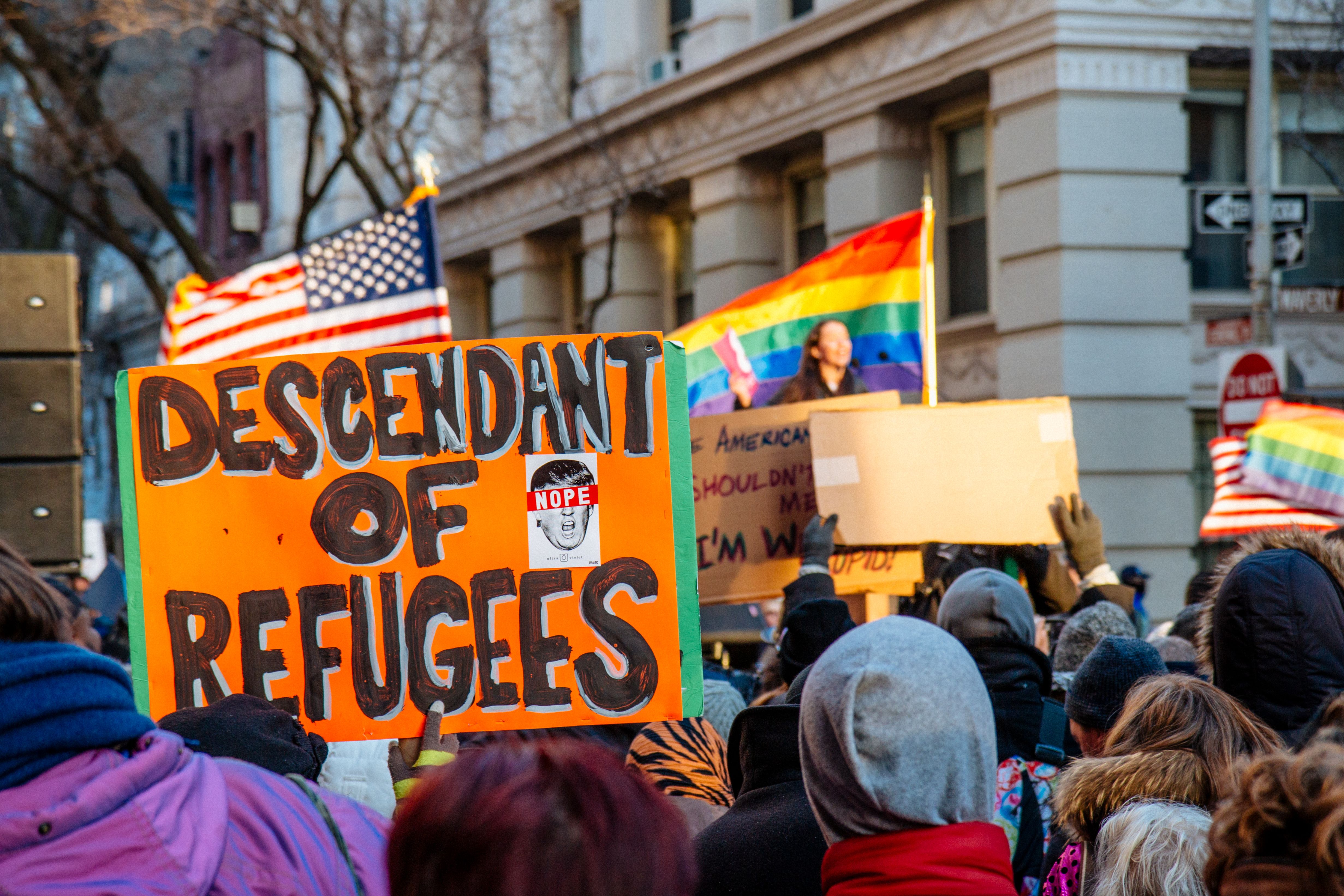 Protester holds orange sign reading 'Descendant of Refugees' at an outdoor rally.