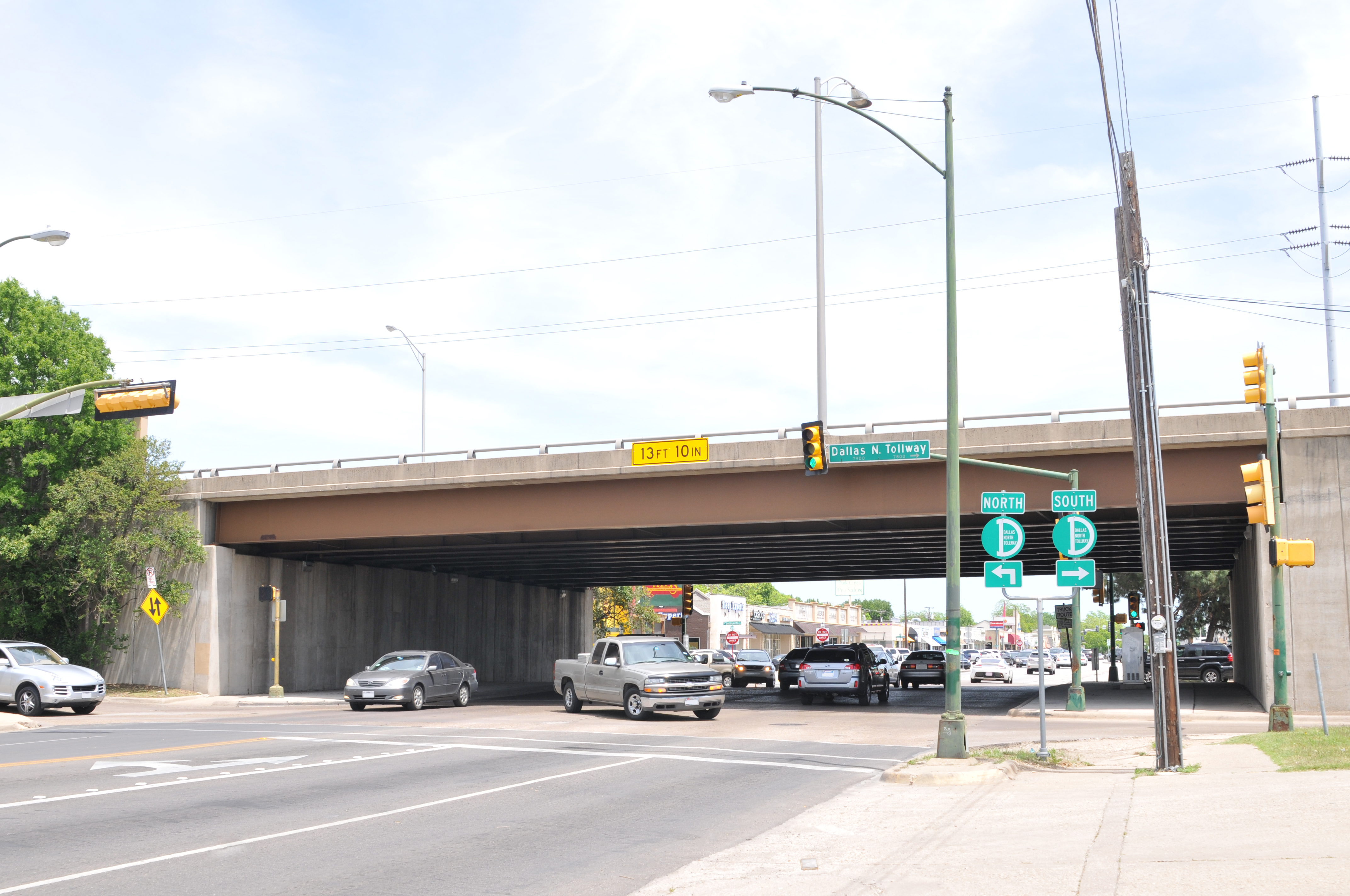Concrete highway overpass spanning an intersection with green directional signs and traffic signals below.
