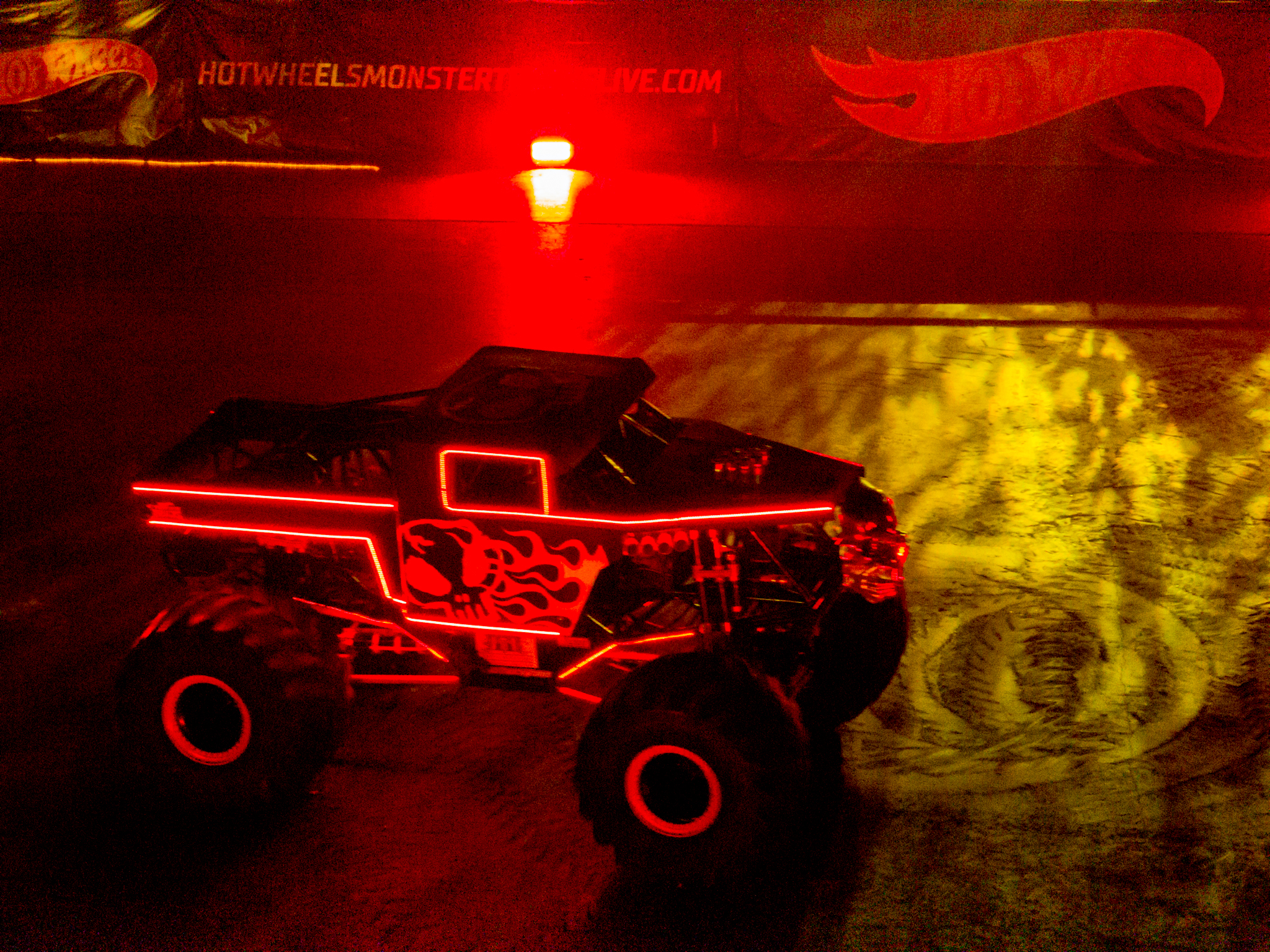 A monster truck outlined in red neon lights sits on a darkened arena floor.