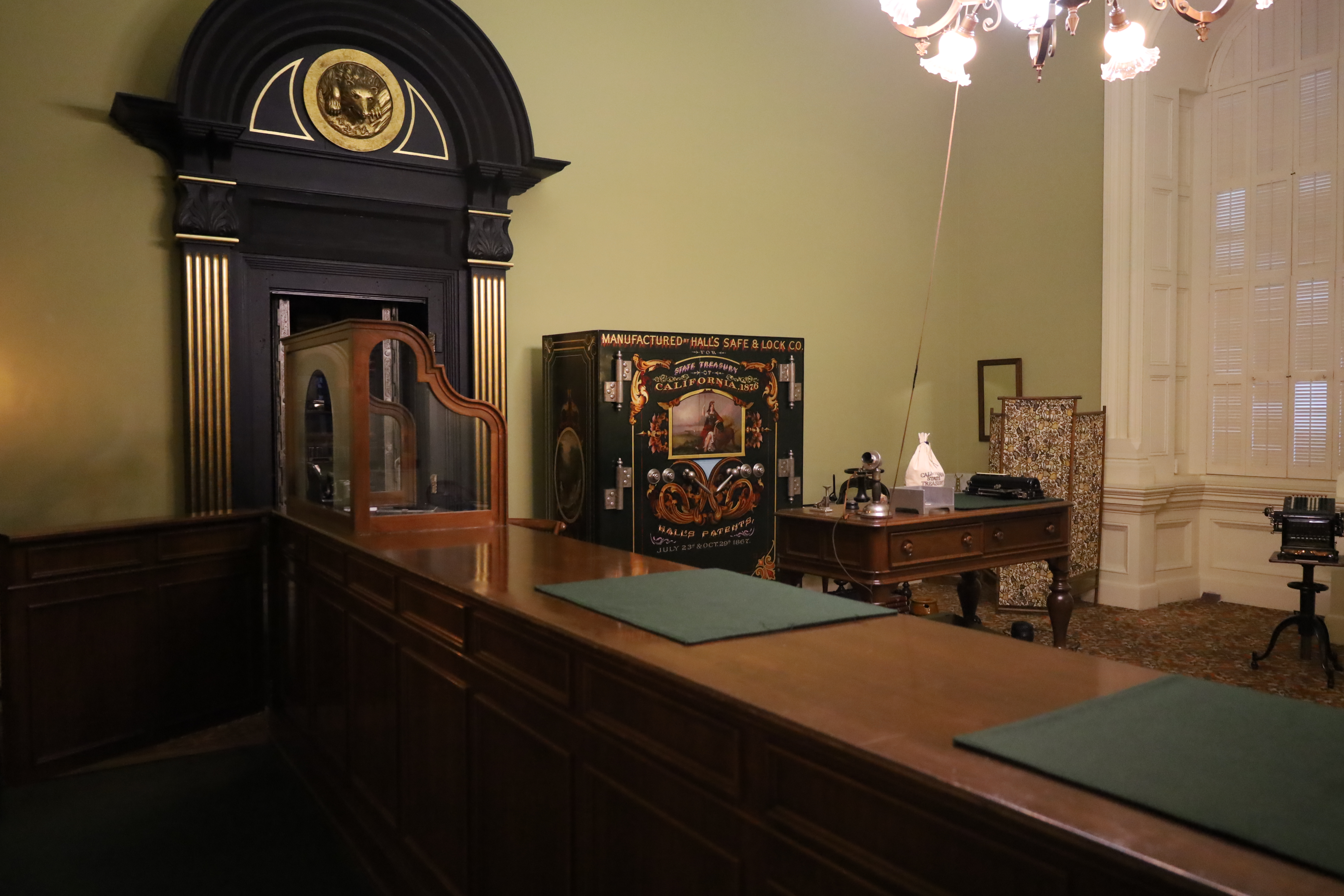 Historic office interior with a long wooden counter, antique safe, and chandelier lighting.