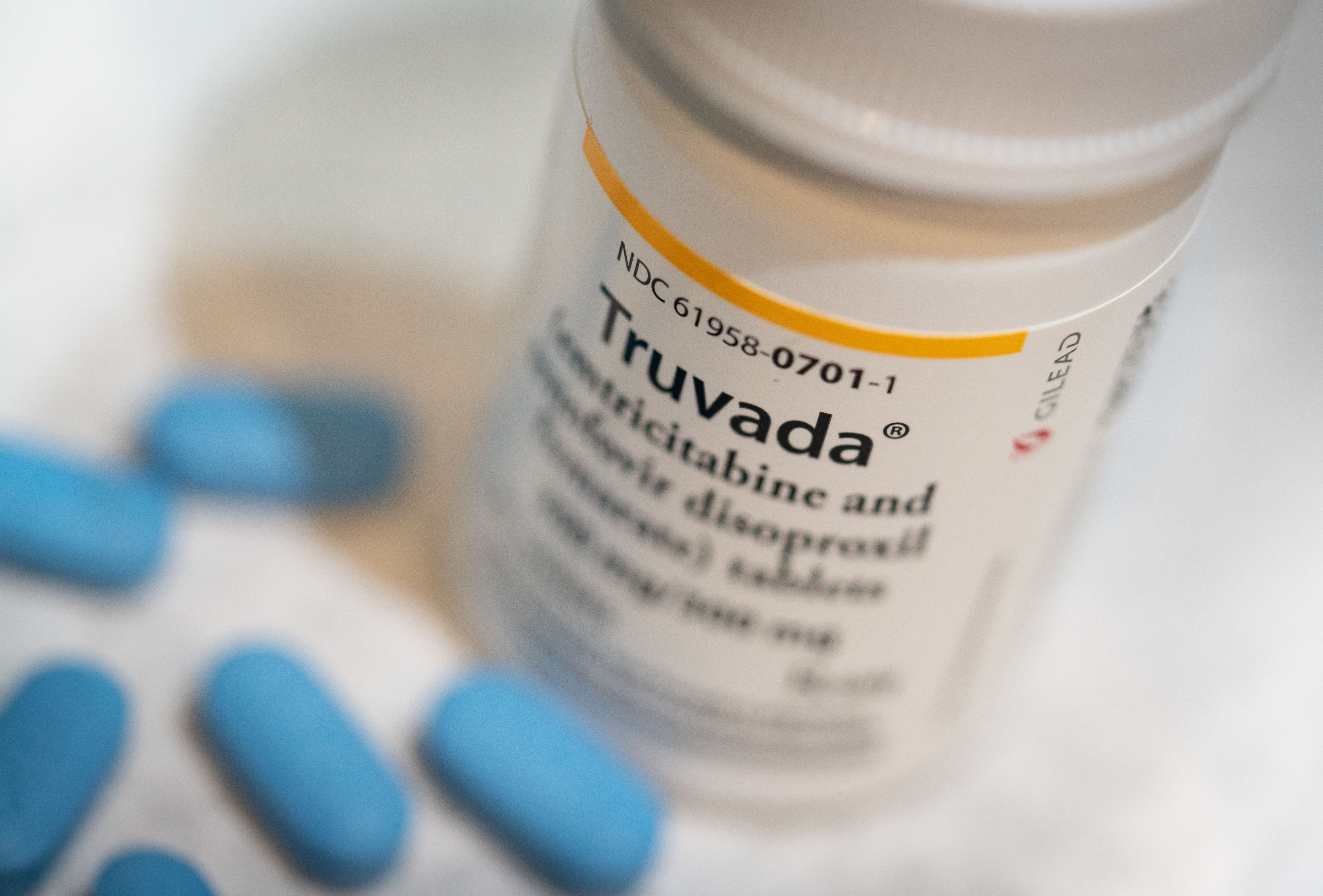 A prescription drug bottle with blue oval pills scattered in front of it.