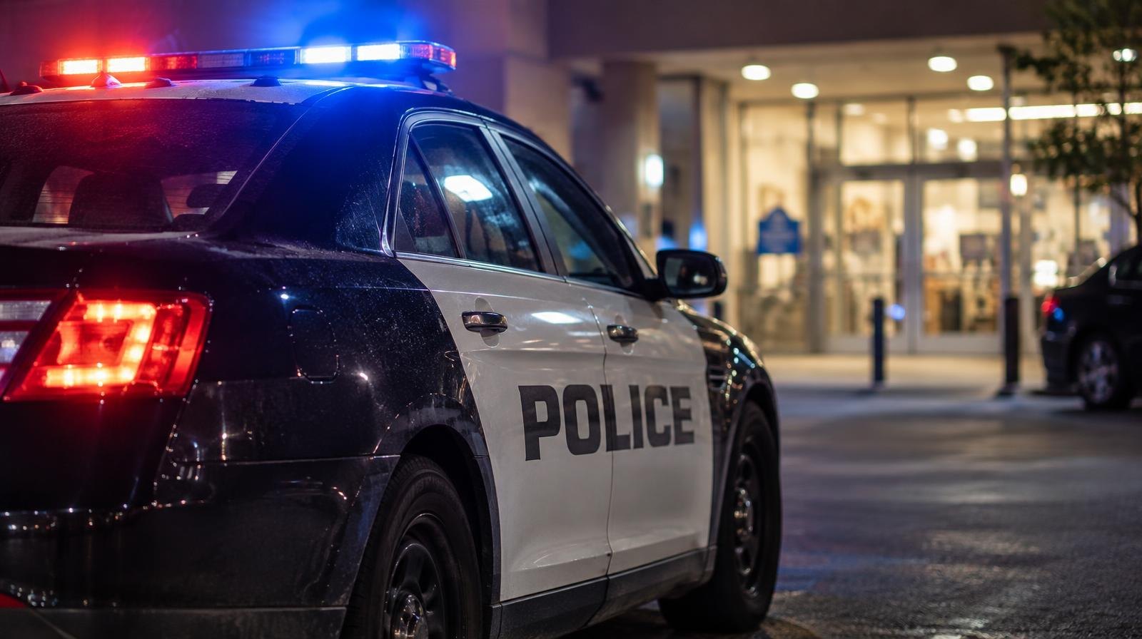 Police cruiser with red and blue emergency lights on outside a building at night.