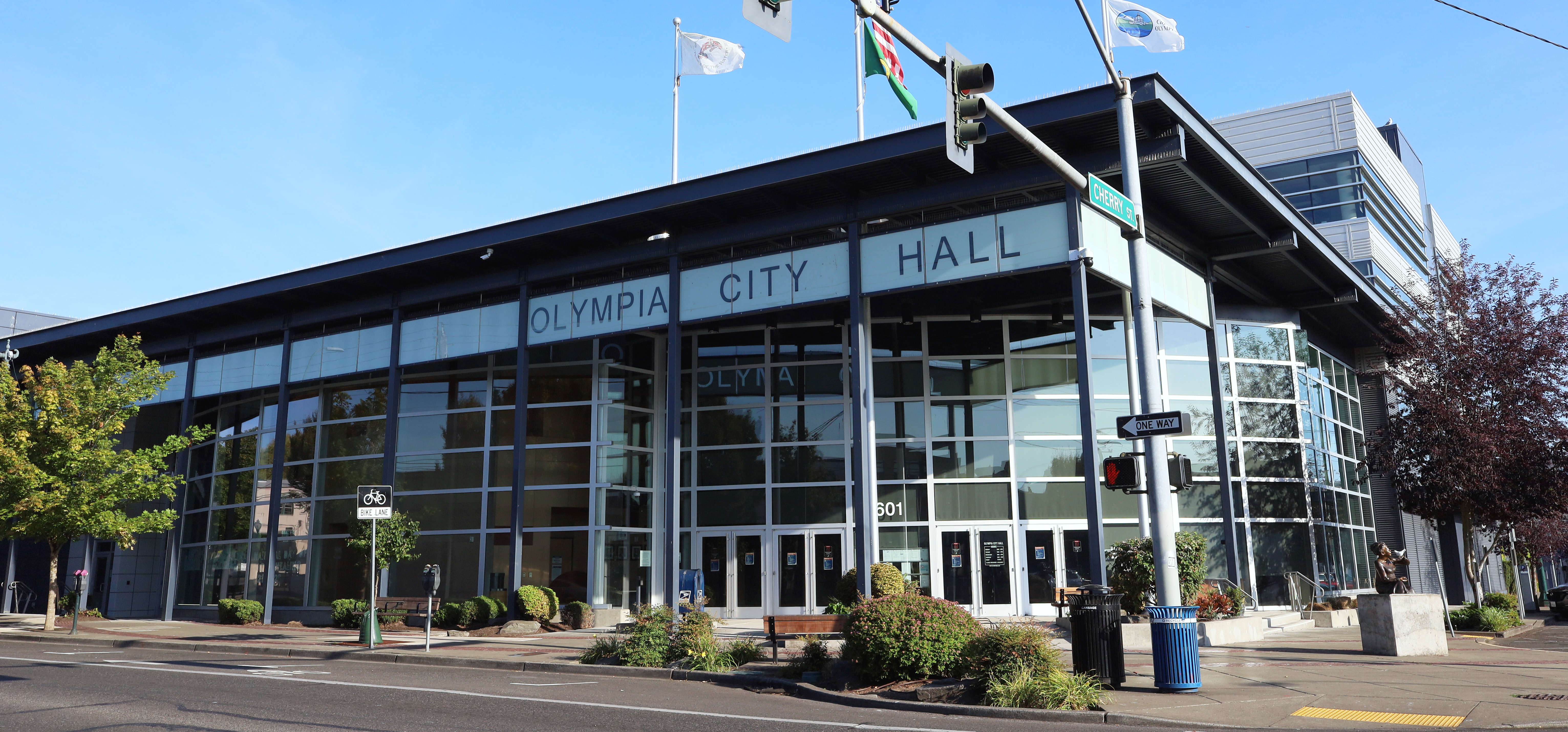 Exterior of Olympia City Hall, a modern glass-facade building with flags on the roof under clear skies.