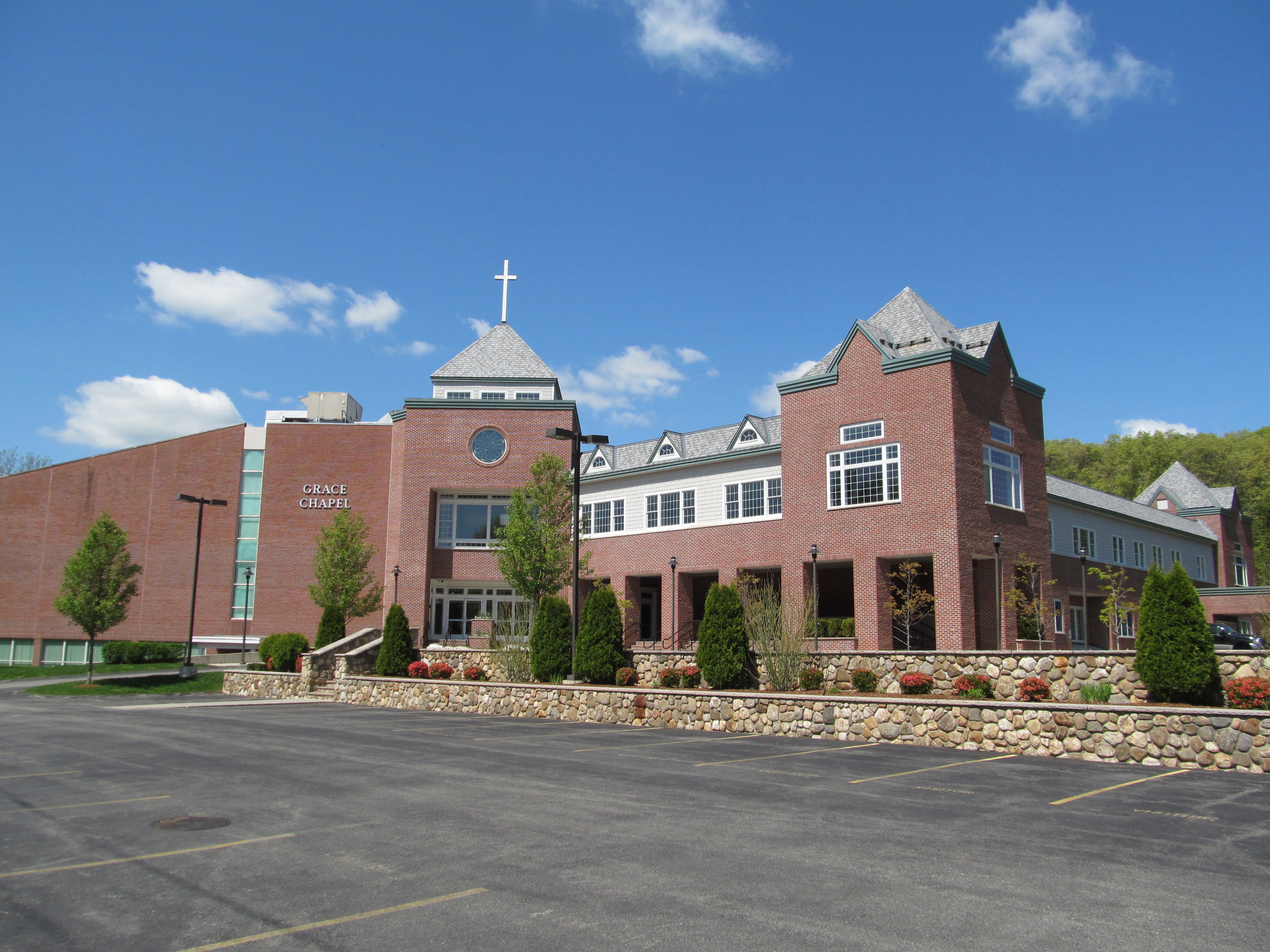 Brick church building with white cross on steeple and a large parking lot in front.