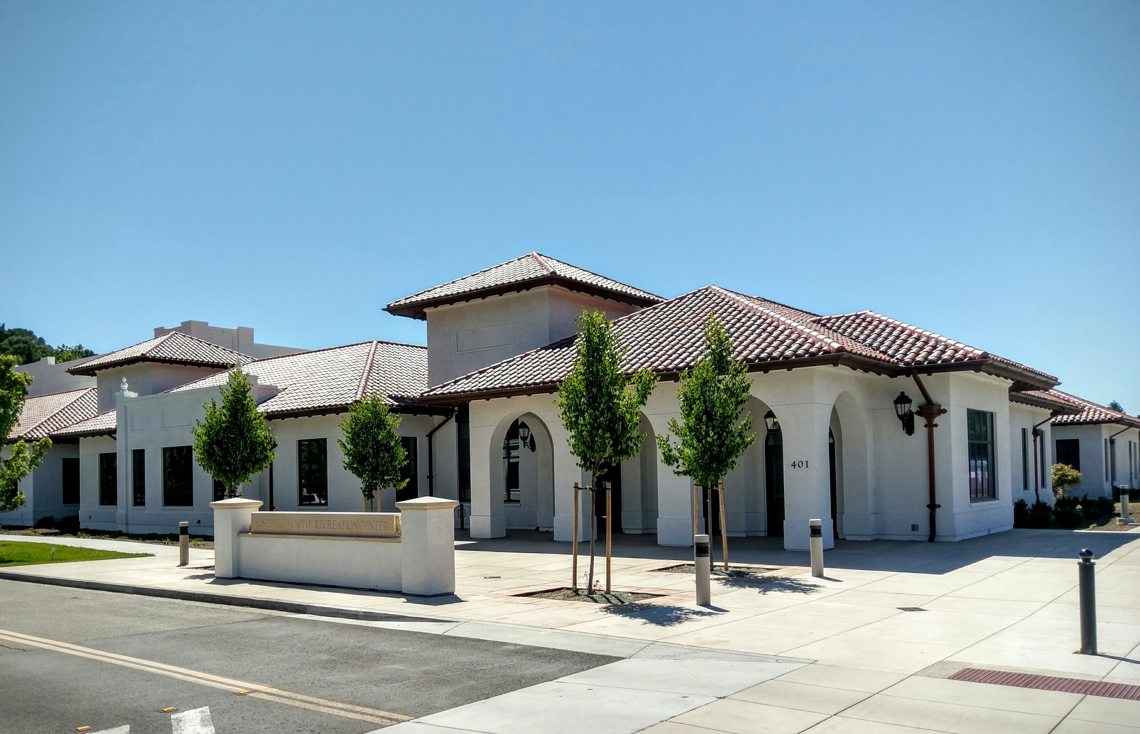 Spanish Colonial Revival building with red tile roof and arched entryways on a sunny day.