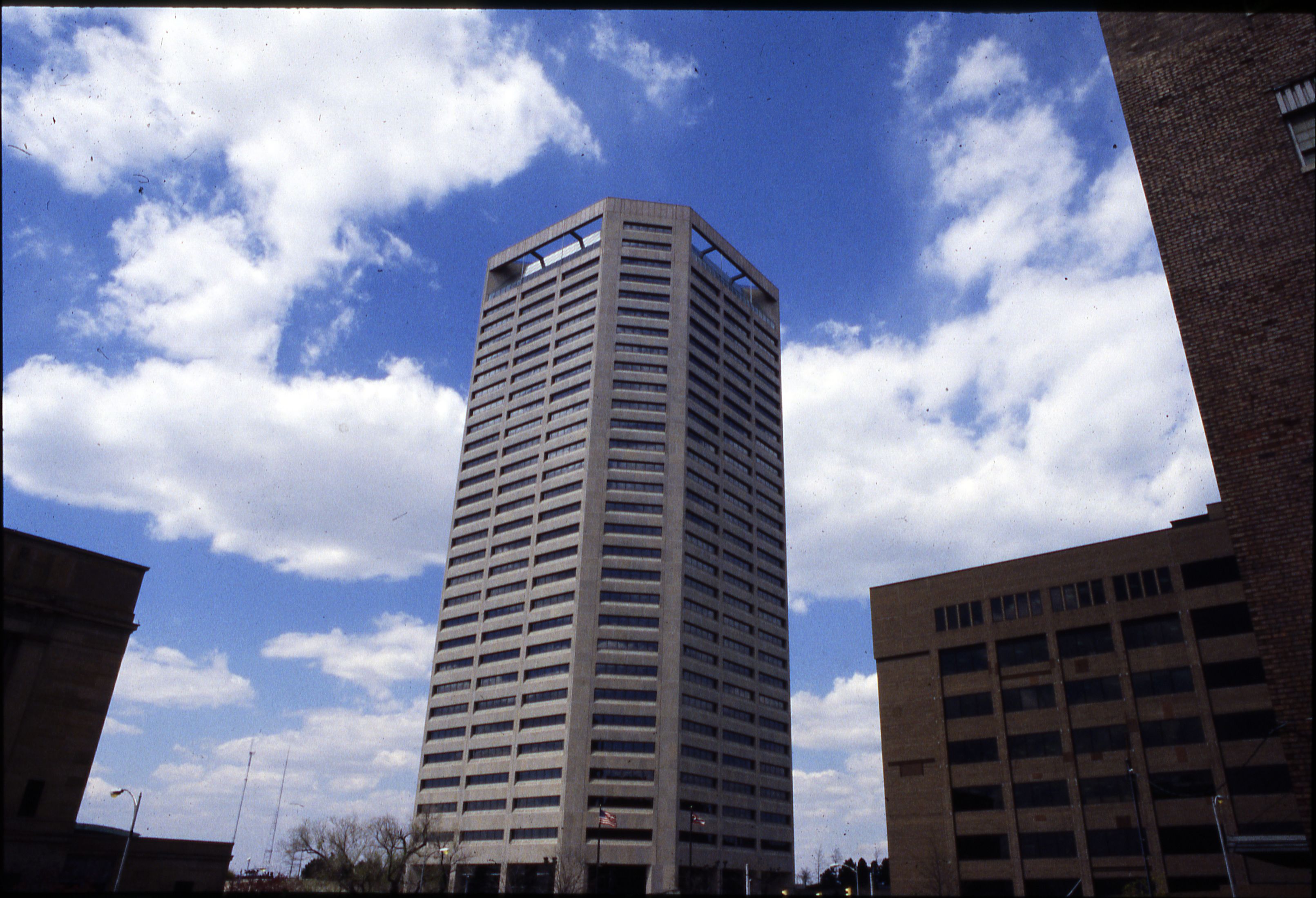 Tall glass-and-concrete office tower rises against a partly cloudy sky.