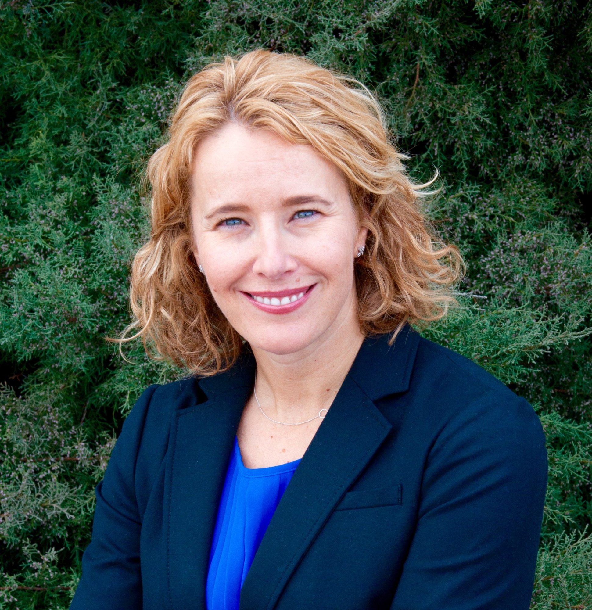 Woman with curly reddish-blonde hair smiling in a professional portrait outdoors.