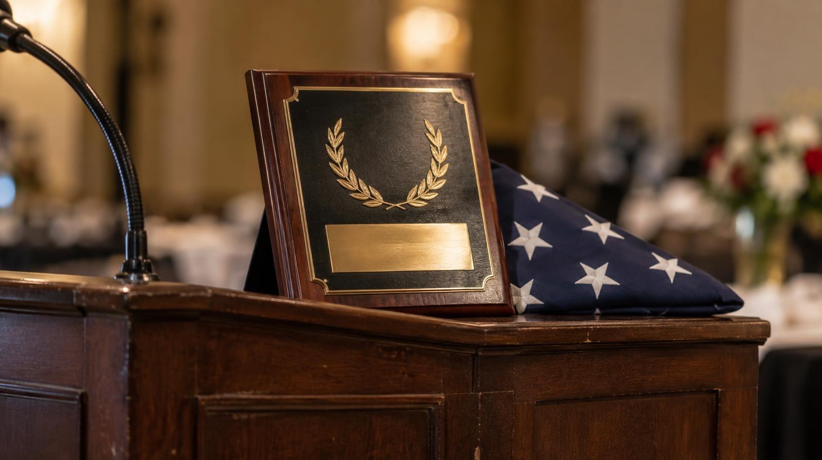 A polished award plaque on a wooden podium beside a folded American flag.