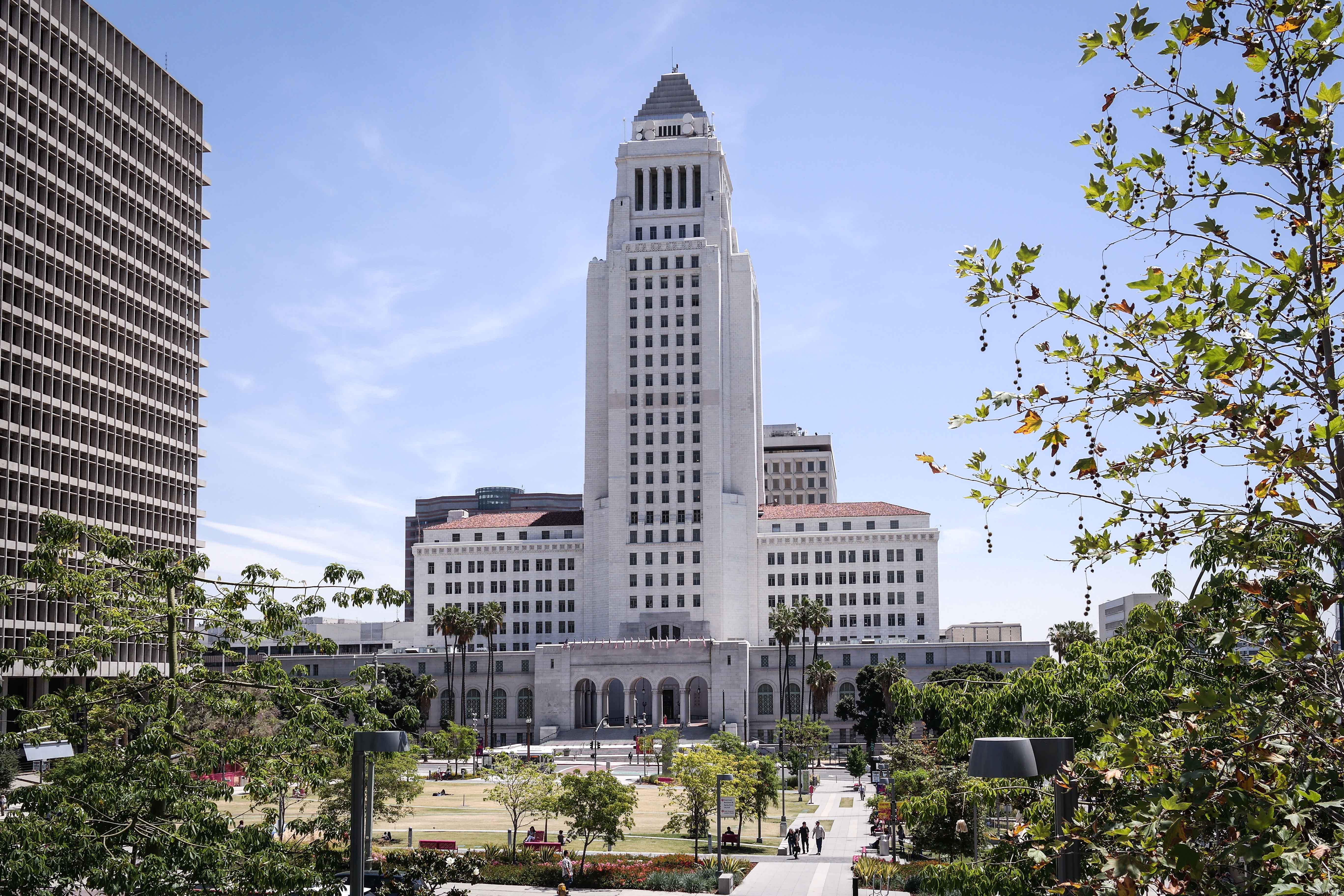 Los Angeles City Hall's stepped white tower rises above a civic plaza lined with palm trees.