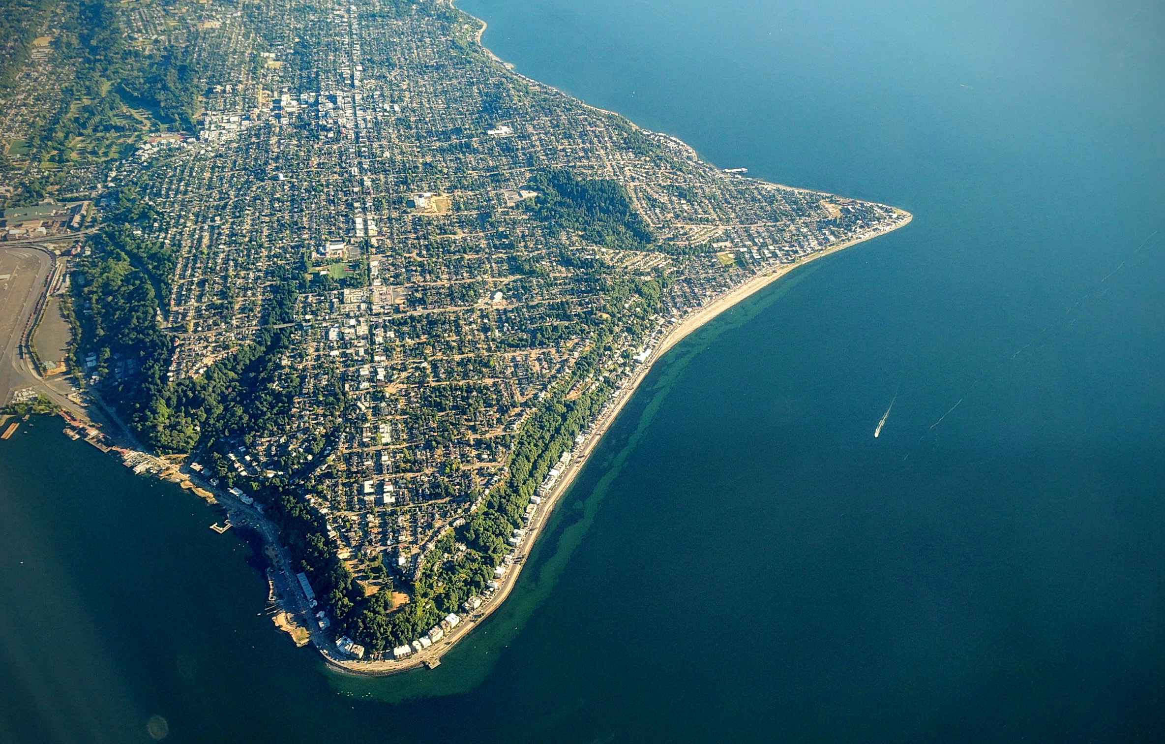 Aerial view of a residential peninsula surrounded by blue water, with a curved beach shoreline visible.