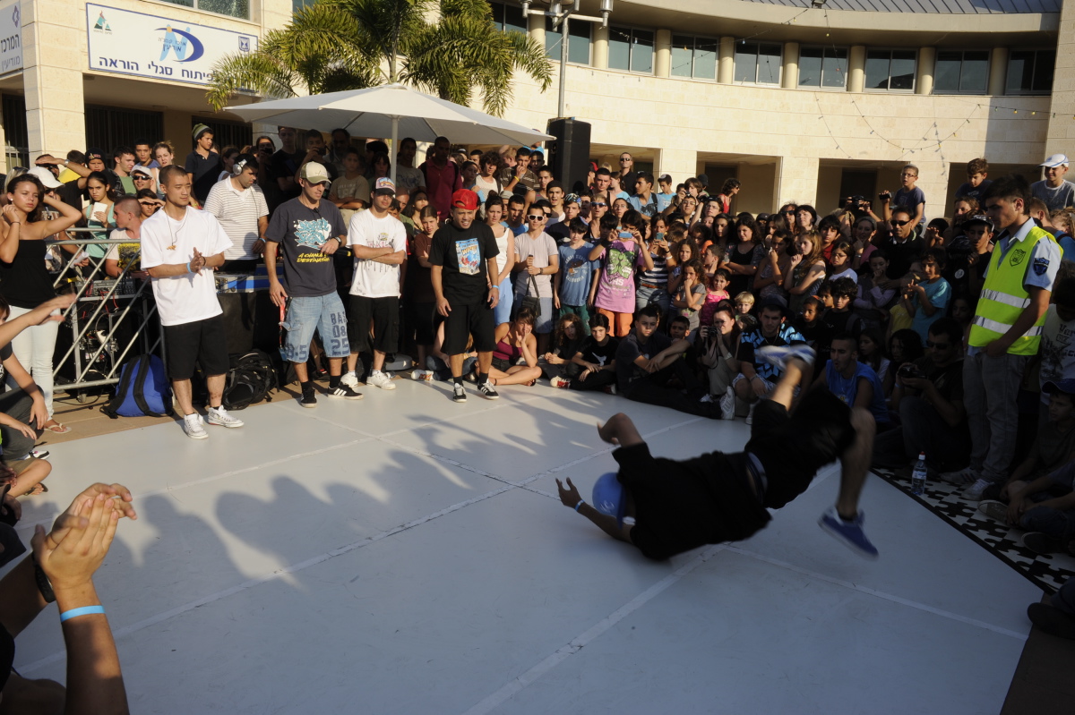 Breakdancer performing a floor move on a white mat before a large crowd of onlookers.
