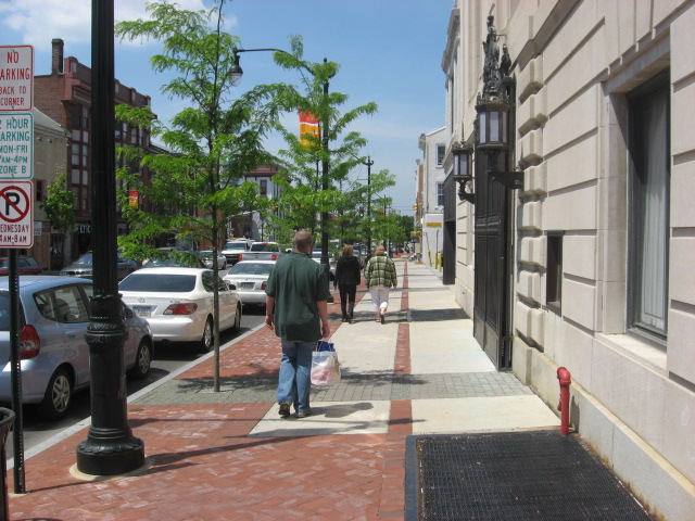 Pedestrians walk along a brick sidewalk on a sunny day in downtown Norristown.