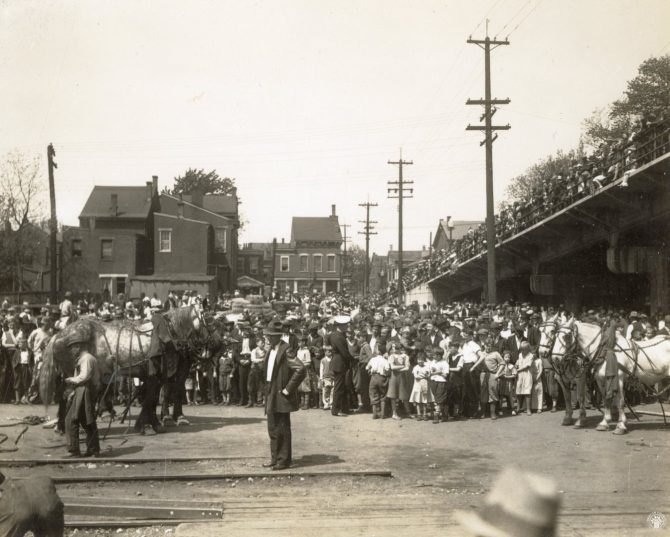 Early 20th-century crowd watching a horse-drawn circus procession on a city street.