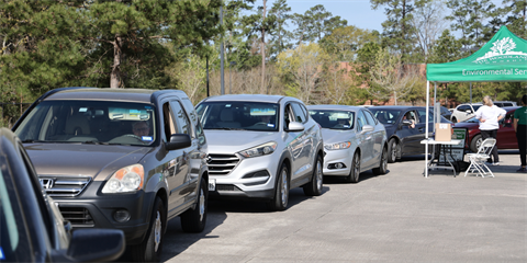 A line of cars queued at an outdoor drive-thru collection event under a green Environmental Services tent.