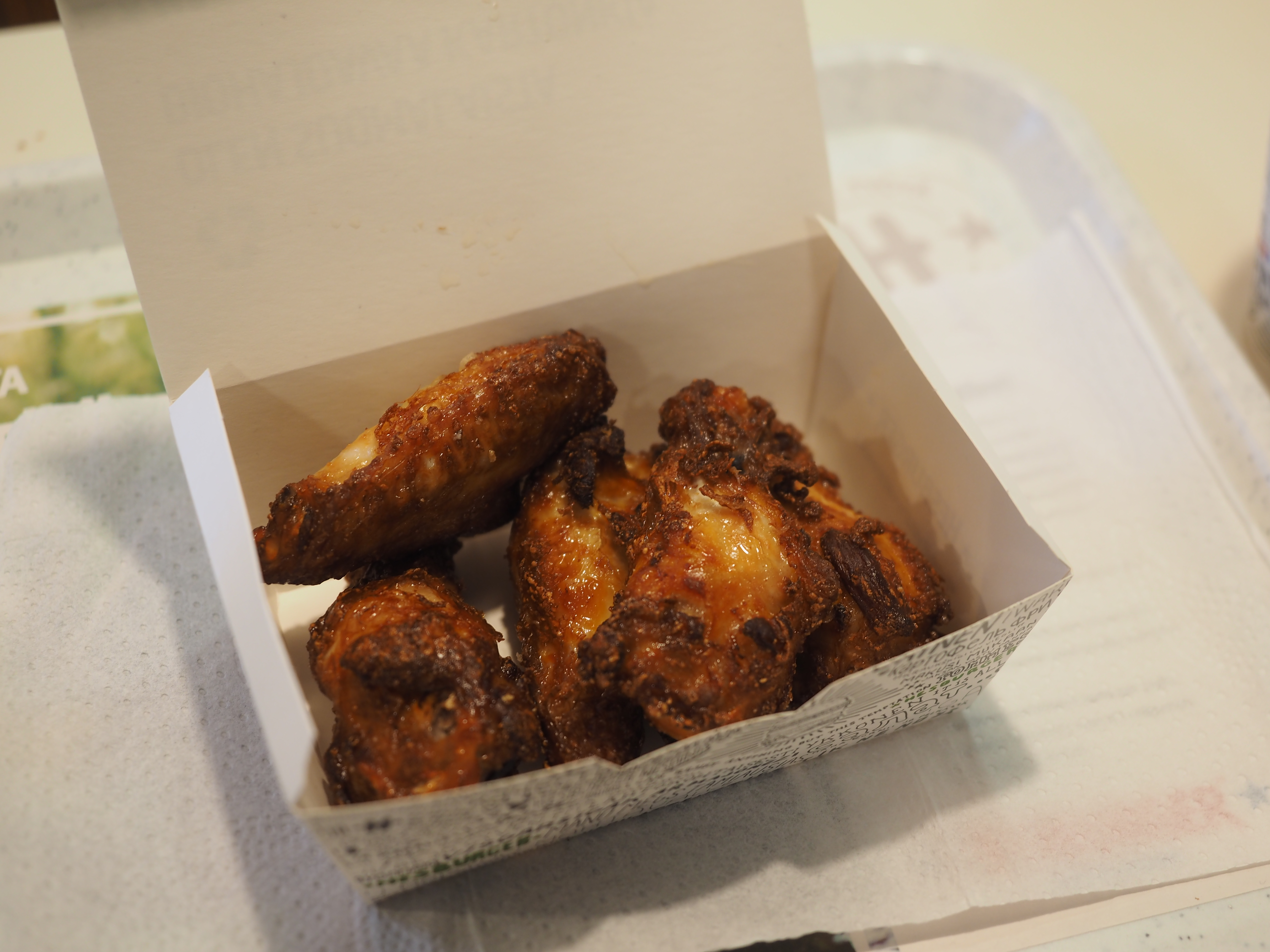 Five sauced chicken wings served in an open white cardboard takeout box.
