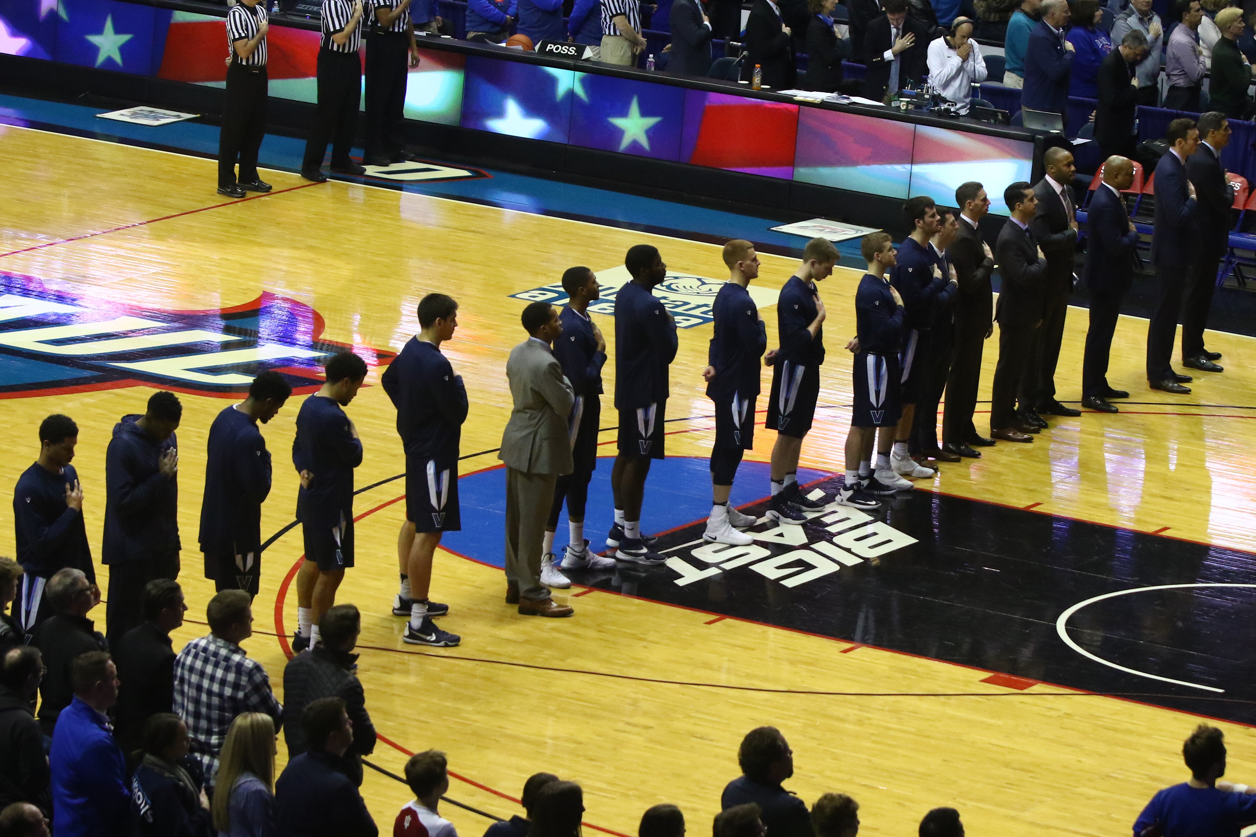 Men's basketball team in dark uniforms lined up on a hardwood court with a Big East logo visible.