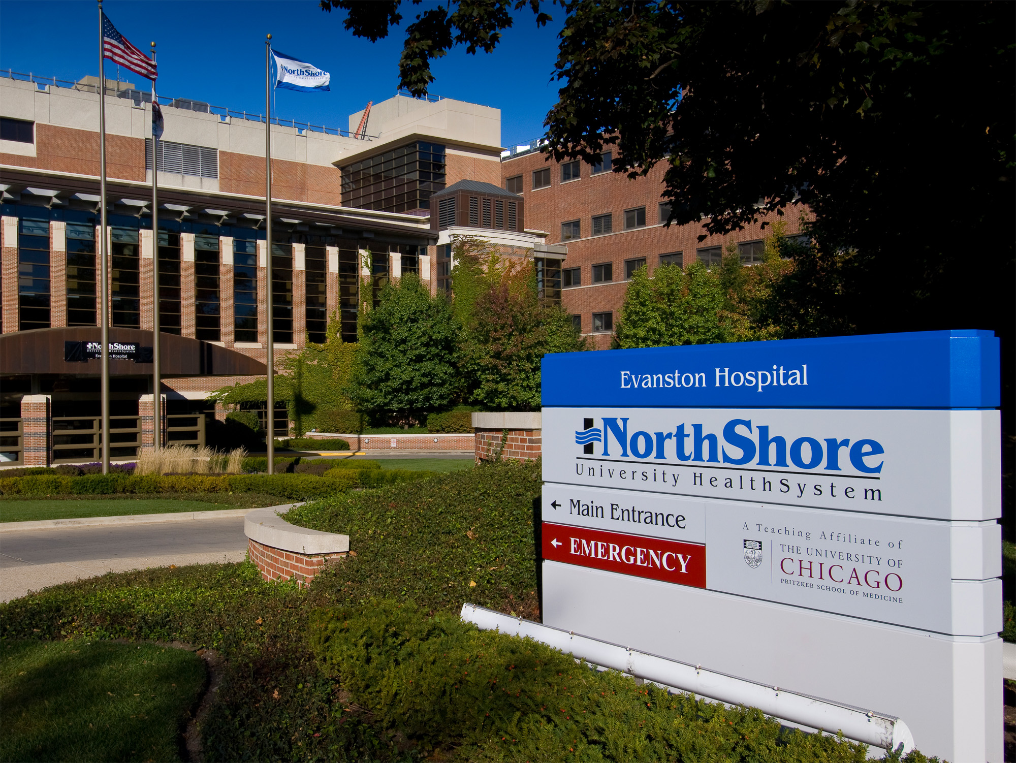 Entrance sign and brick facade of a hospital building with flags and landscaping