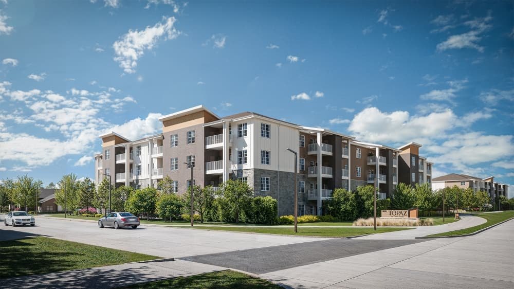 Rendering of a four-story apartment building with balconies, stone facade, and a monument sign near a curved road.