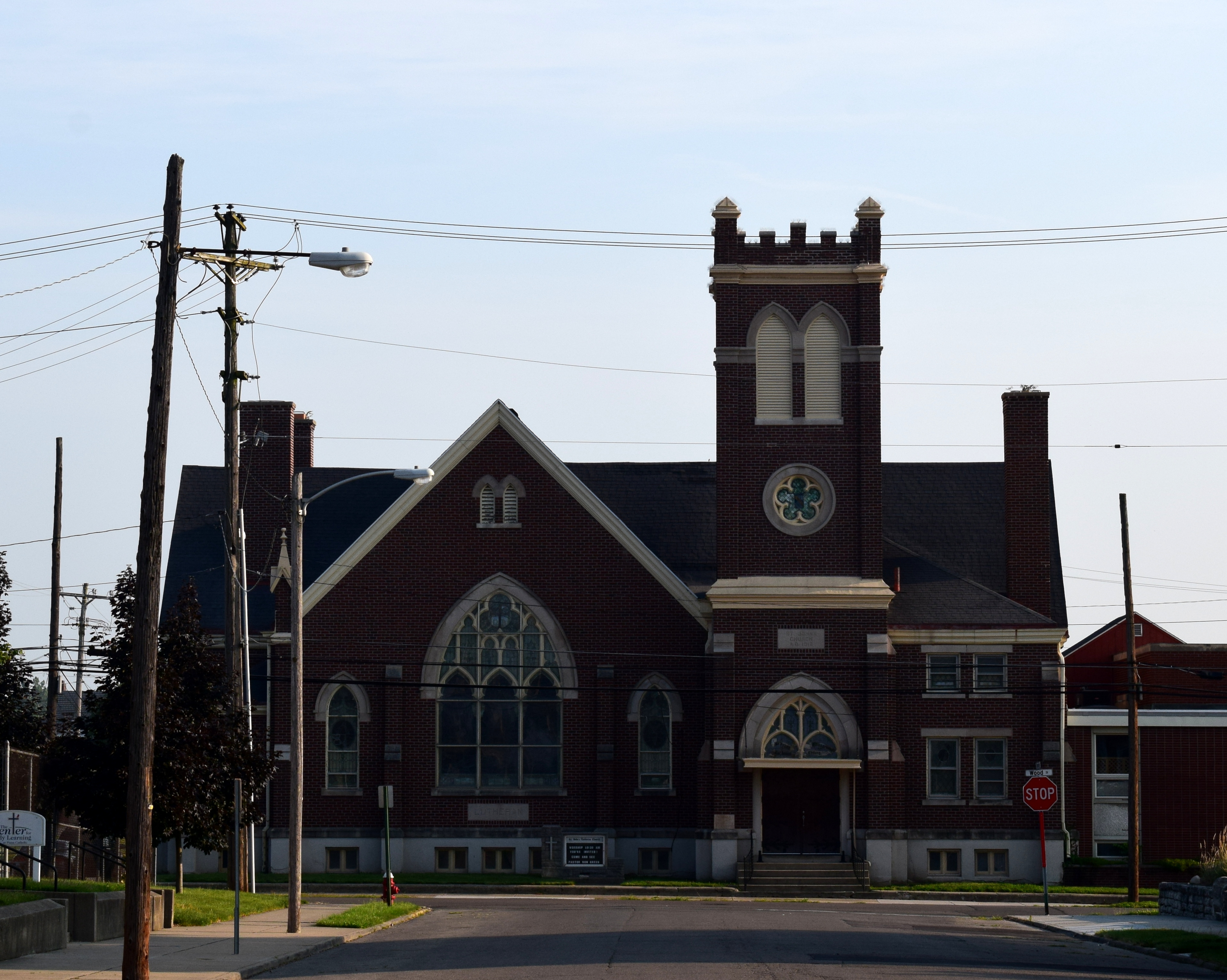 Red brick Lutheran church with a square bell tower and arched stained-glass windows at a street corner.
