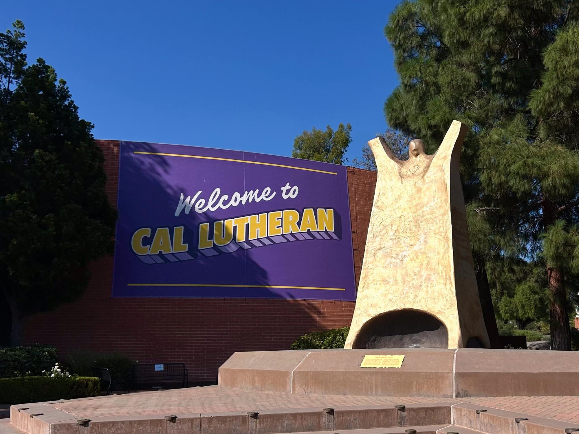 Purple and gold welcome banner on a brick building with a large stone sculpture in the foreground.