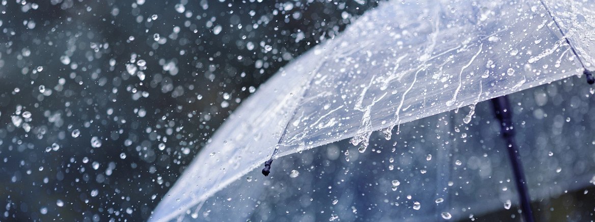 A clear umbrella held under heavy rainfall with water droplets splashing around it.