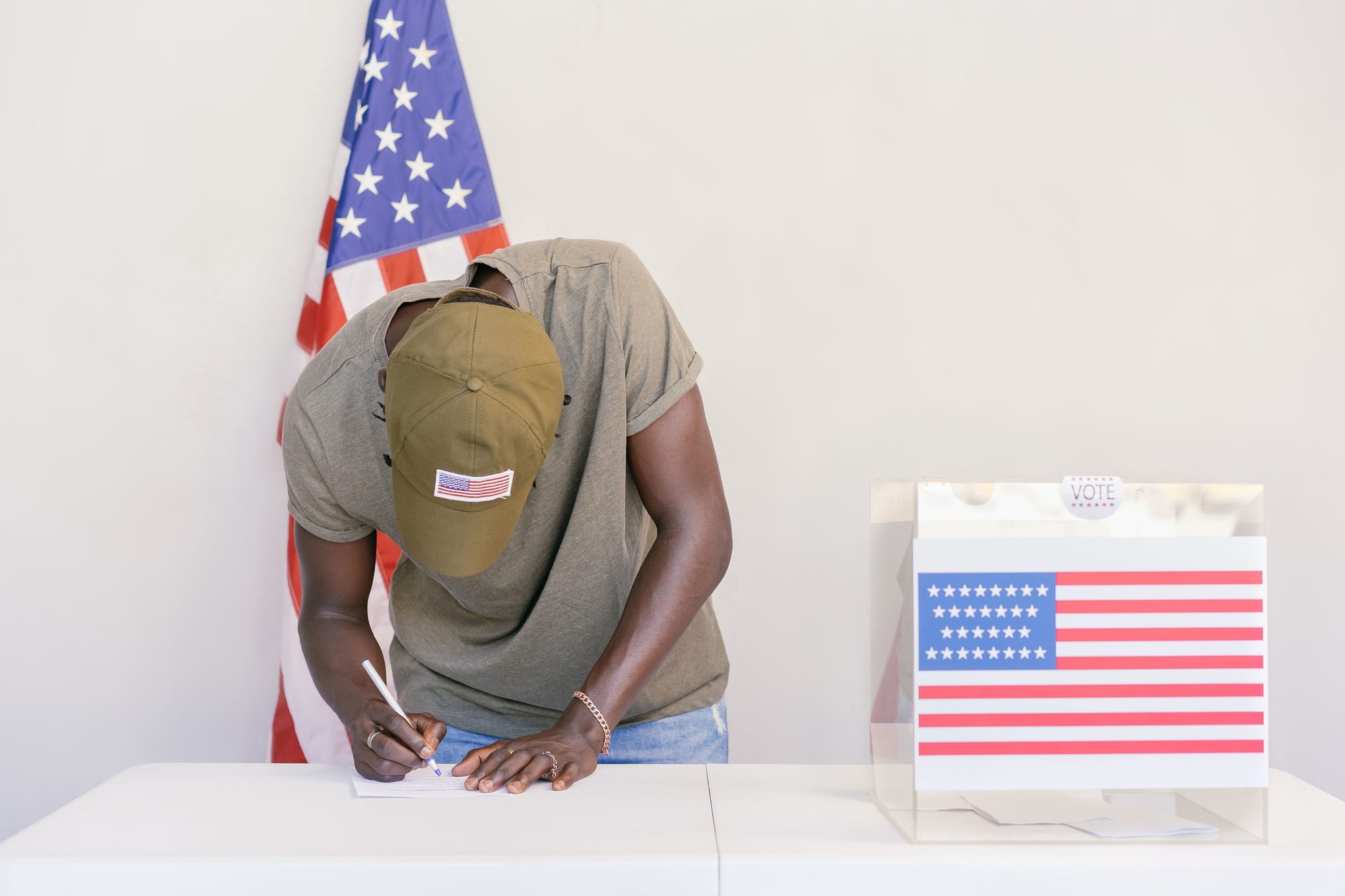 Man casting vote at polling station with American flag in background.