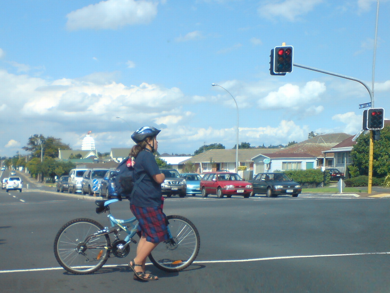 Helmeted cyclist with a backpack pushing a bicycle across an intersection at a red light.