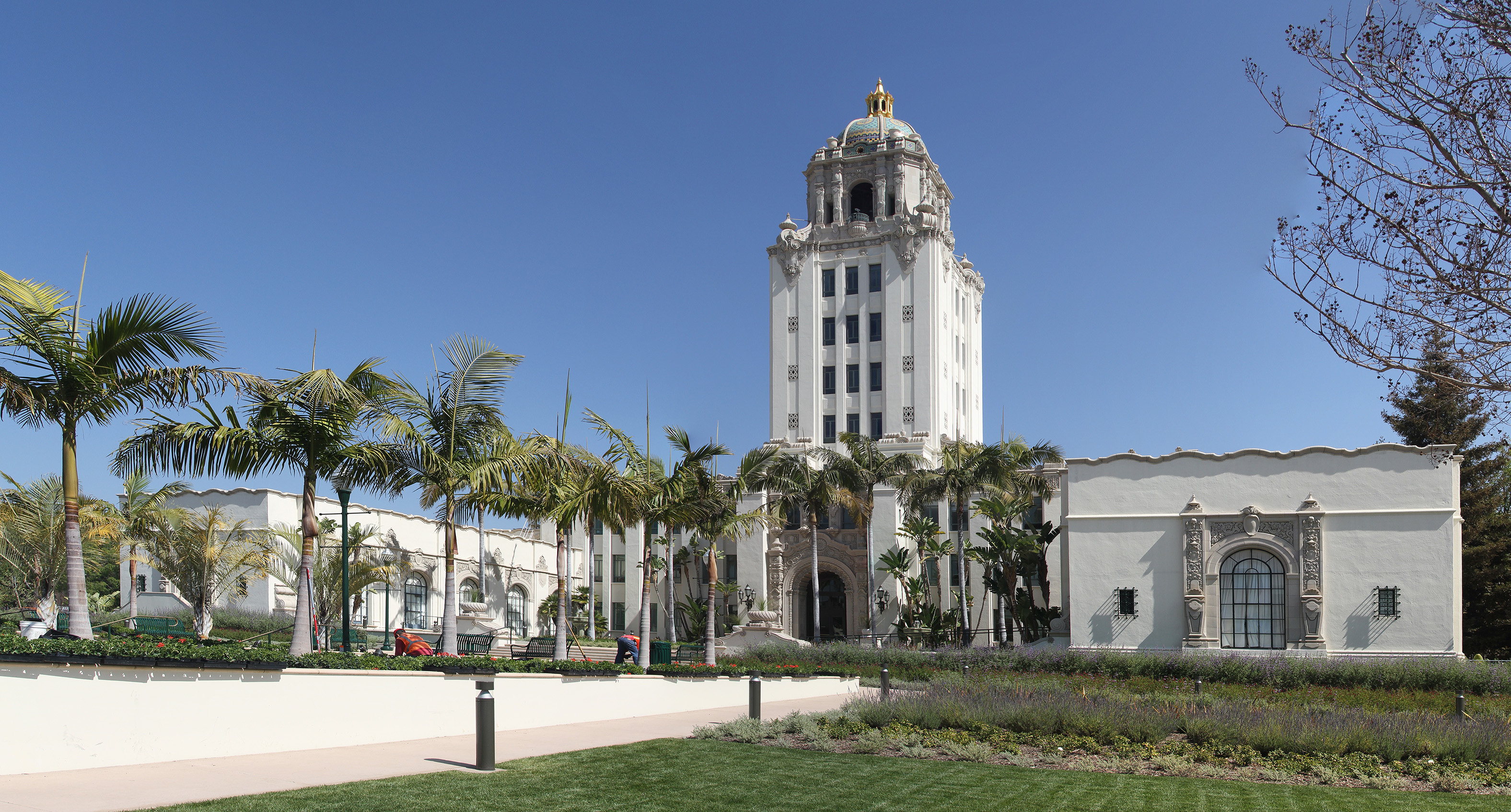 White Spanish Colonial Revival city hall building with gold dome and palm trees.