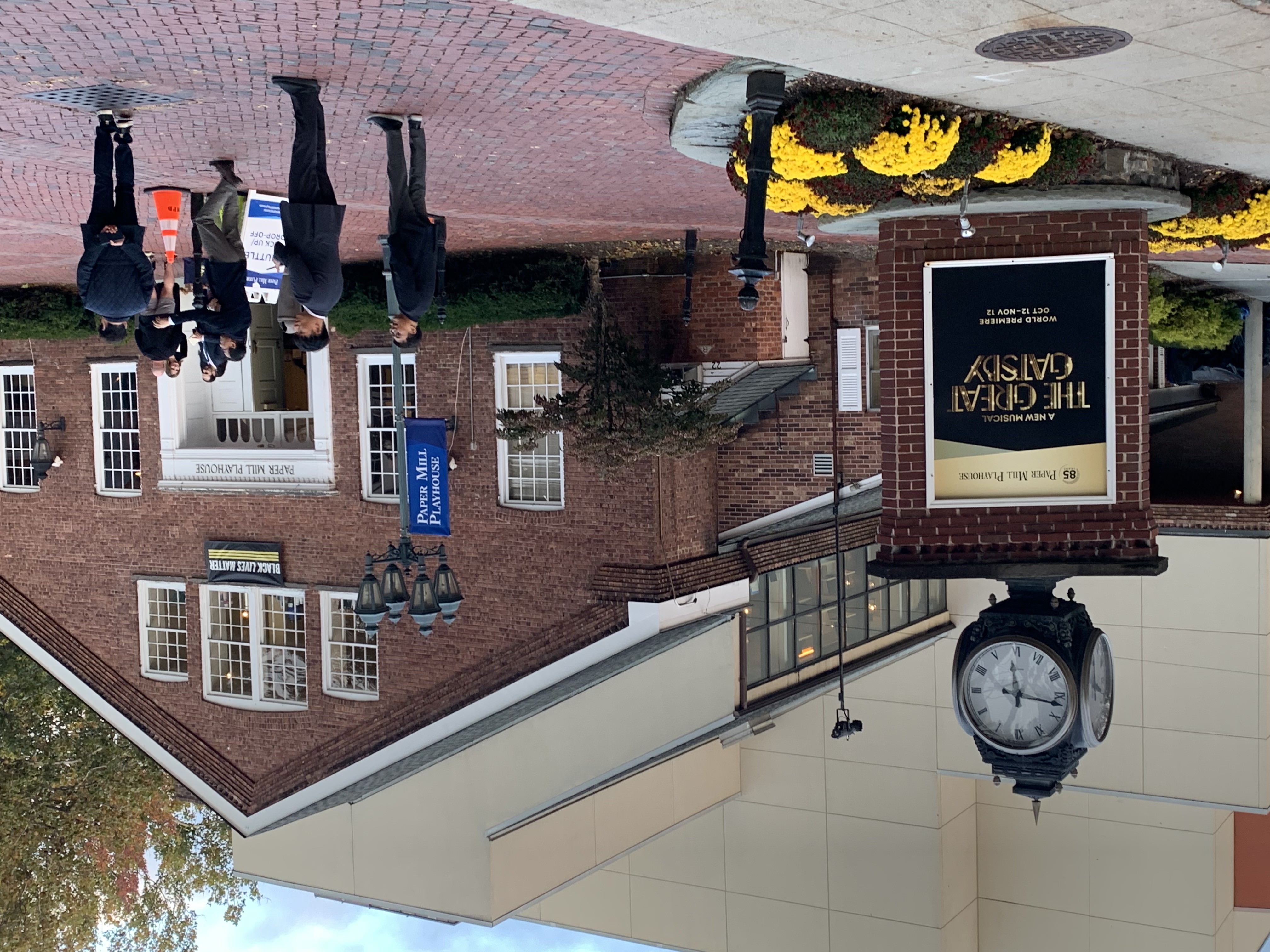 Brick theater building with marquee sign and street clock, people gathered outside on a plaza.
