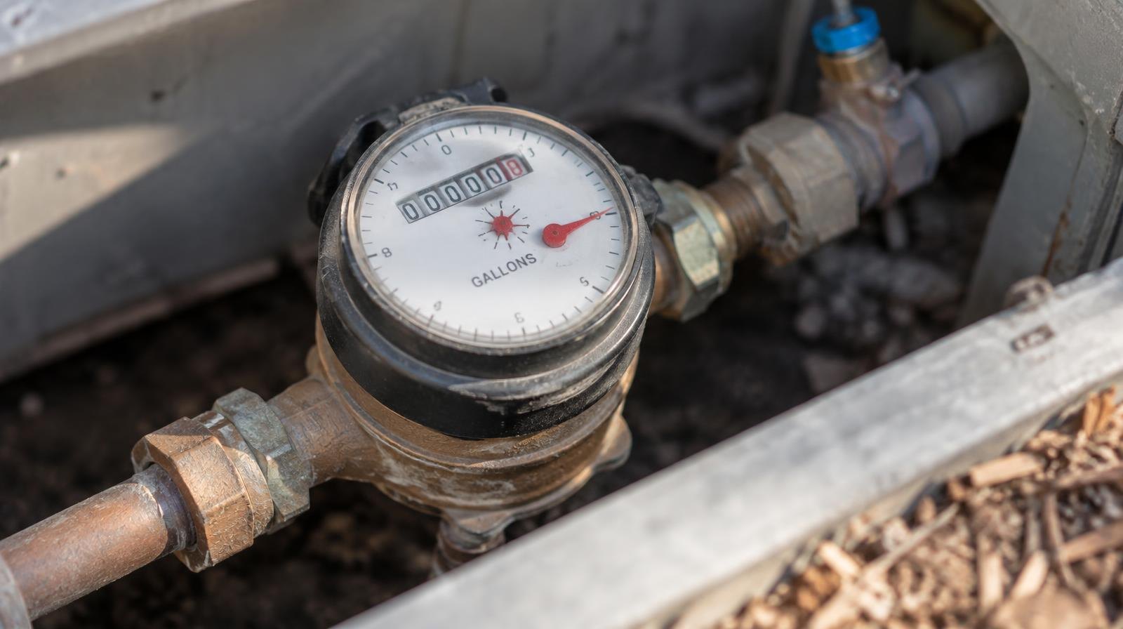 Close-up of a residential water meter with a dial gauge and copper pipe fittings.