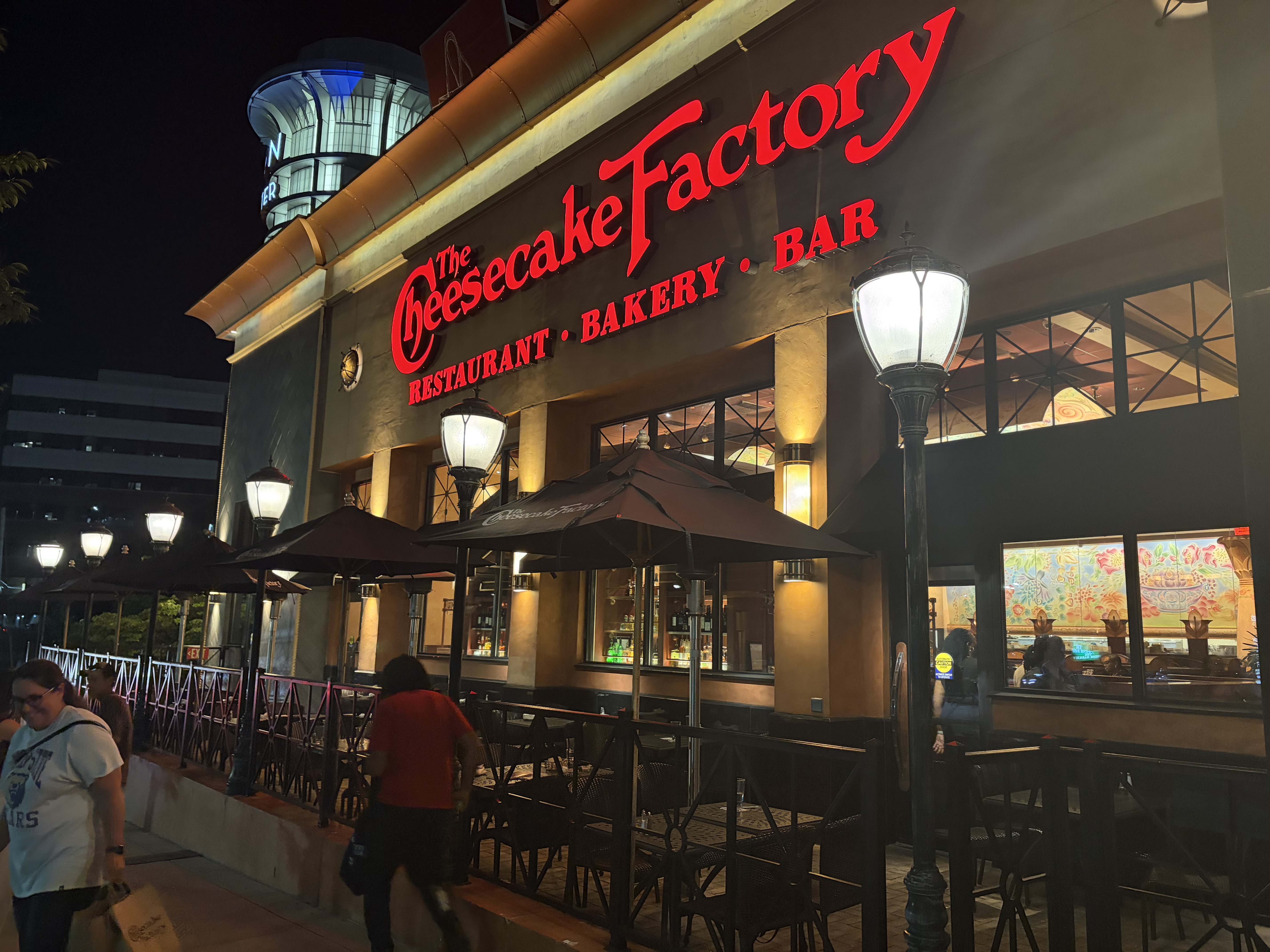 Illuminated Cheesecake Factory restaurant exterior at night with patio seating.