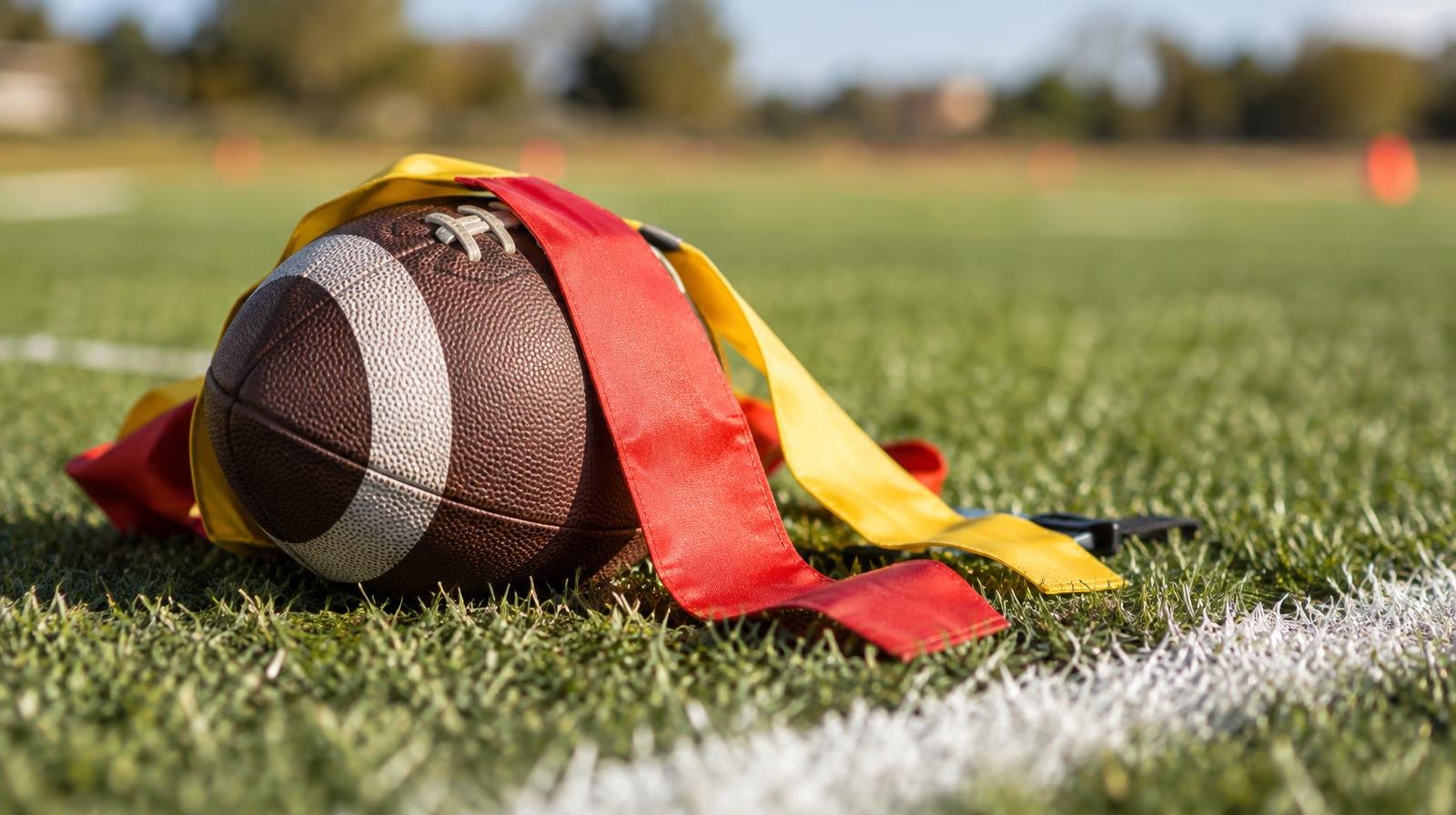 A football with colorful flag belts resting on green grass near a white yard line.
