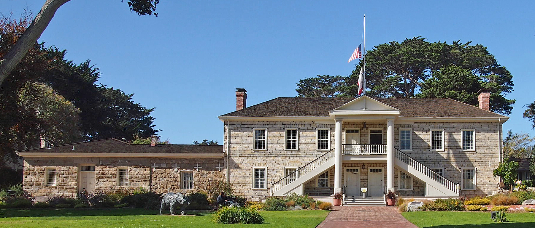 Historic stone civic building with white columns and an American flag on a green lawn.